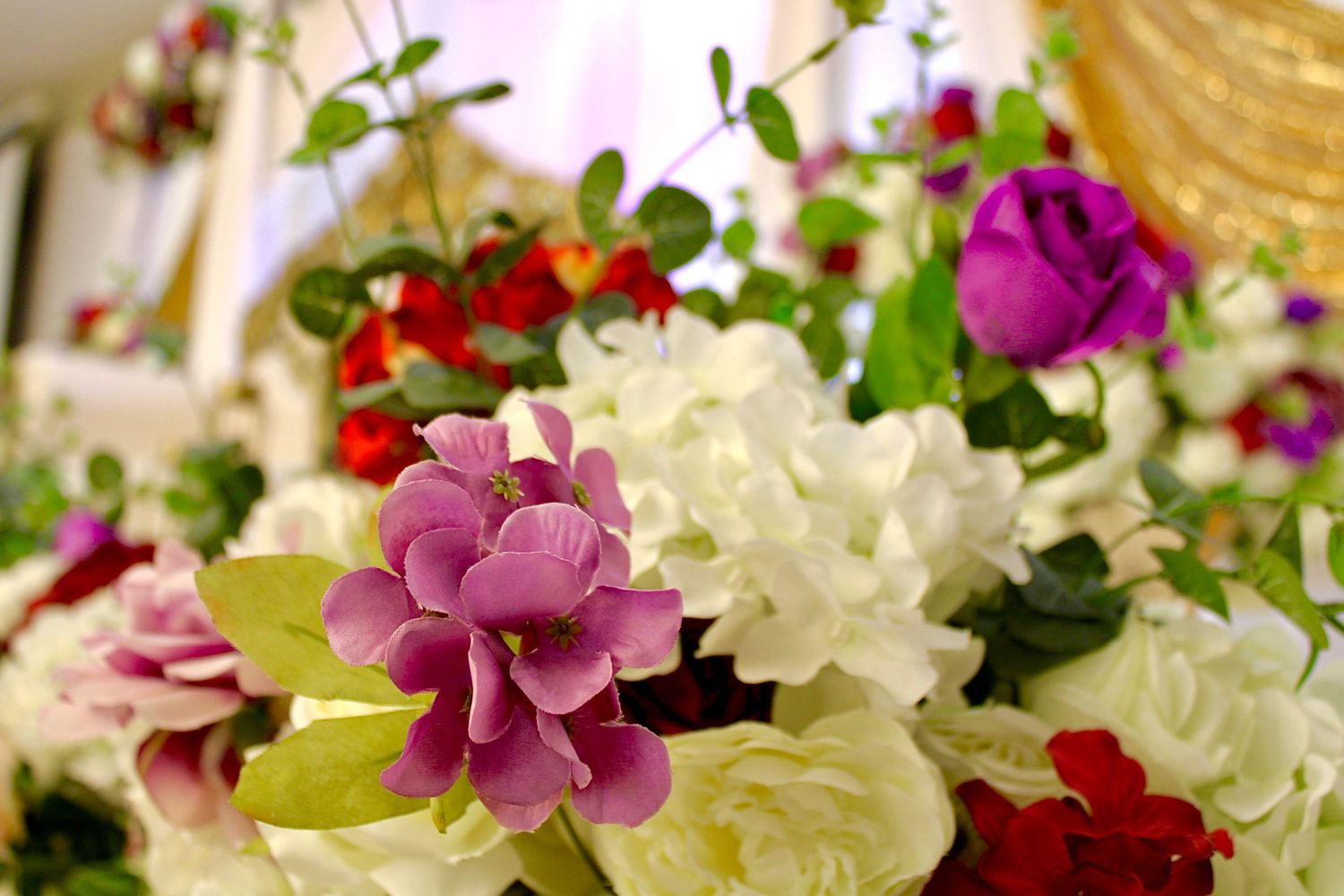 A vibrant floral arrangement featuring pink, purple, red and white roses with delicate greenery accents in soft focus.