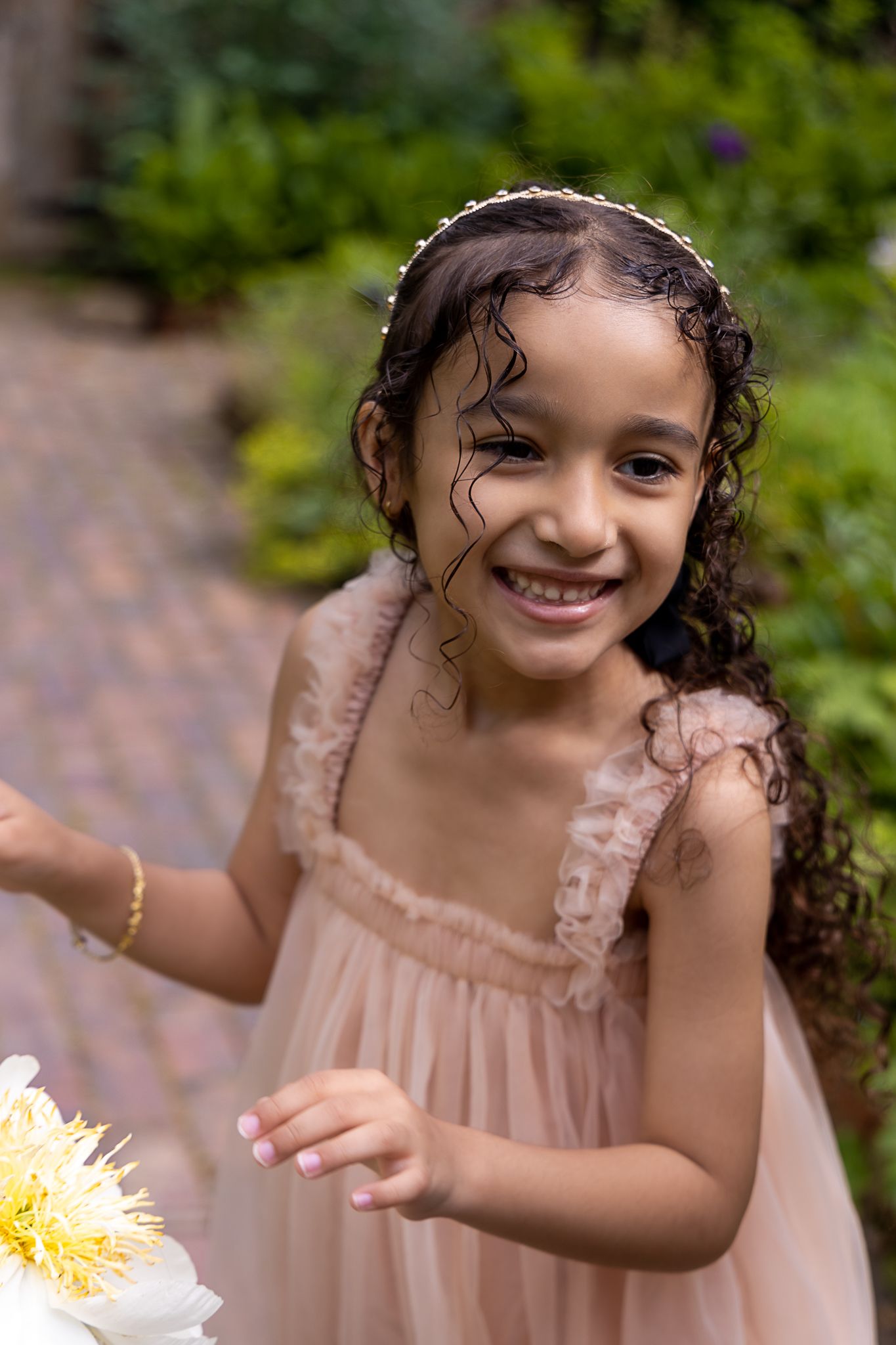 Young child in a pink dress smiles while standing in a garden setting.