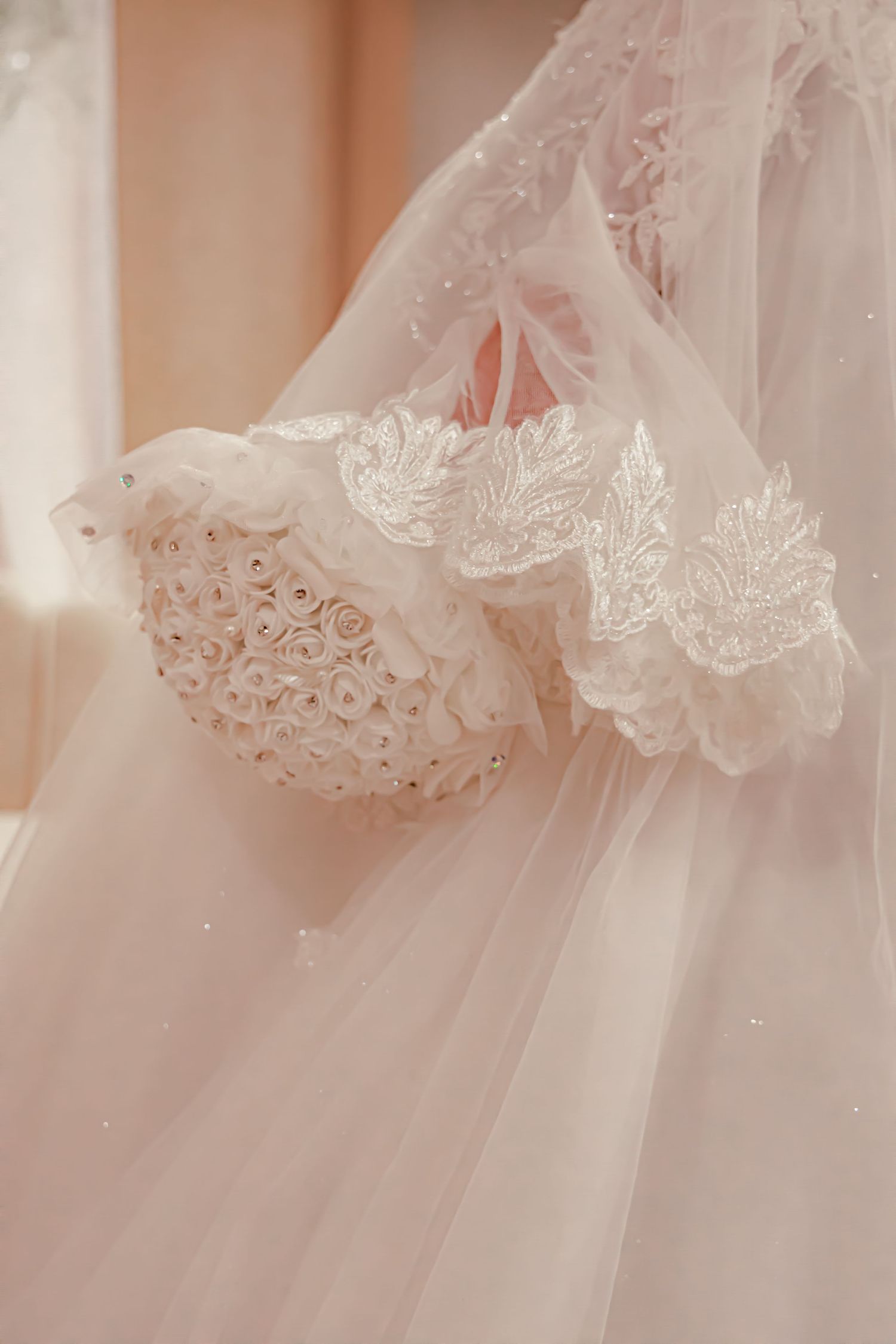Close-up detail of delicate lace and tulle fabric on a white wedding dress sleeve with intricate floral embroidery.
