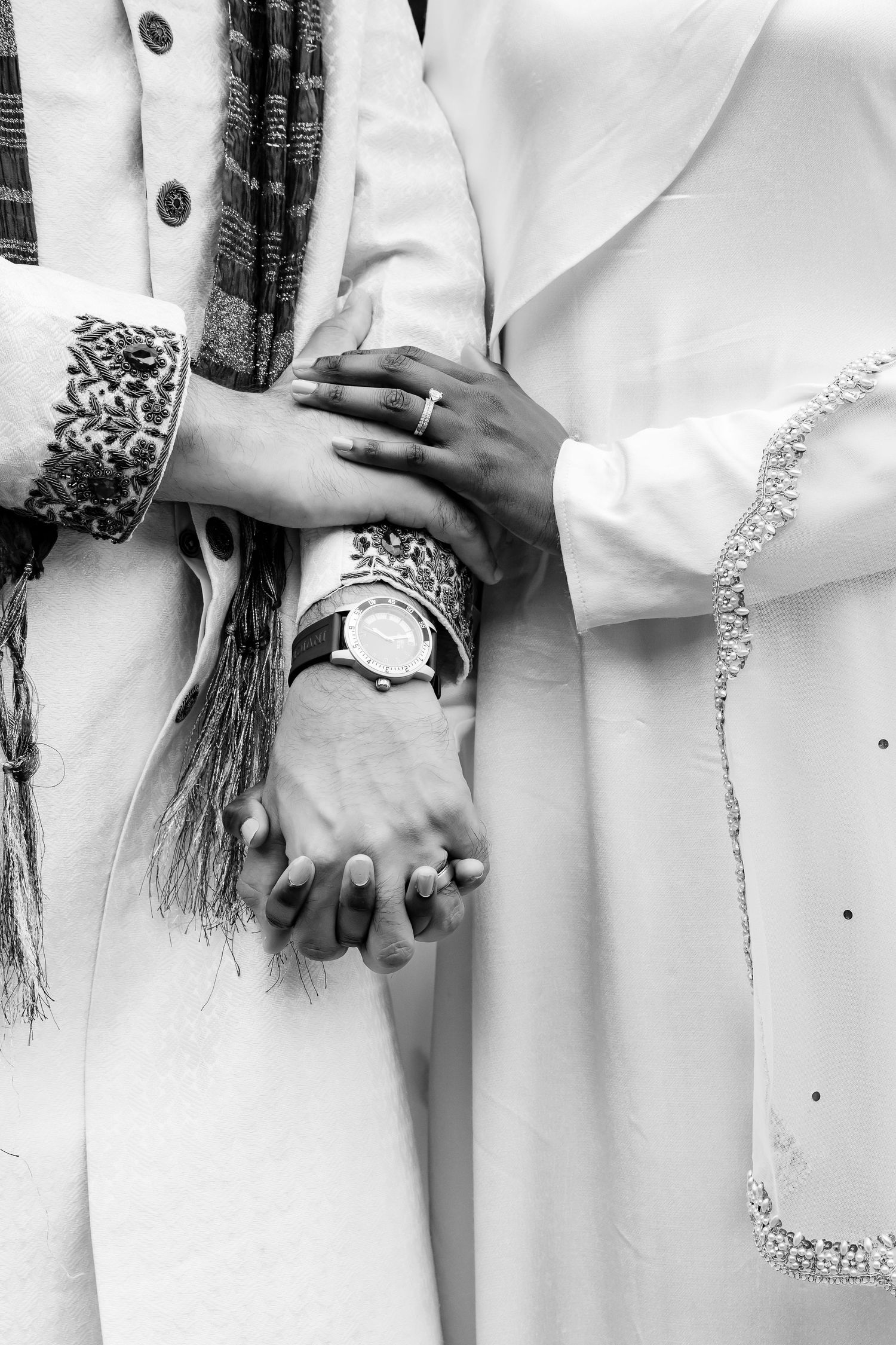 Black and white close-up of clasped hands wearing rings and bracelets with white clothing details. | PHL, PA Wedding Photographer