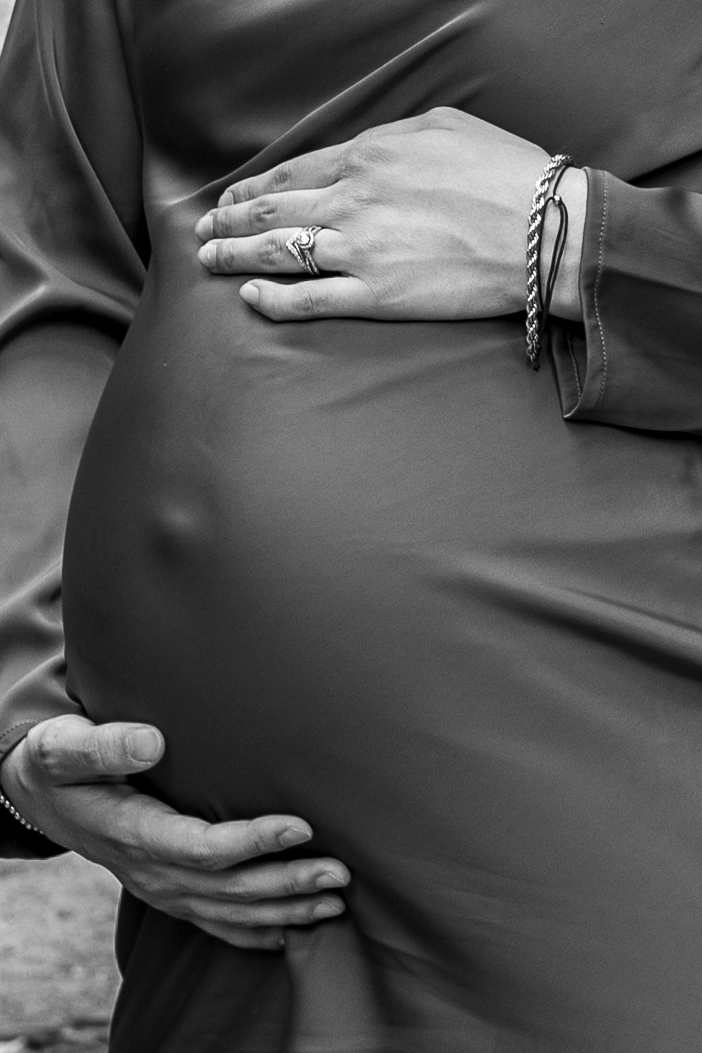 Black and white close-up of hands cradling a pregnant belly showing jewelry and fabric details.