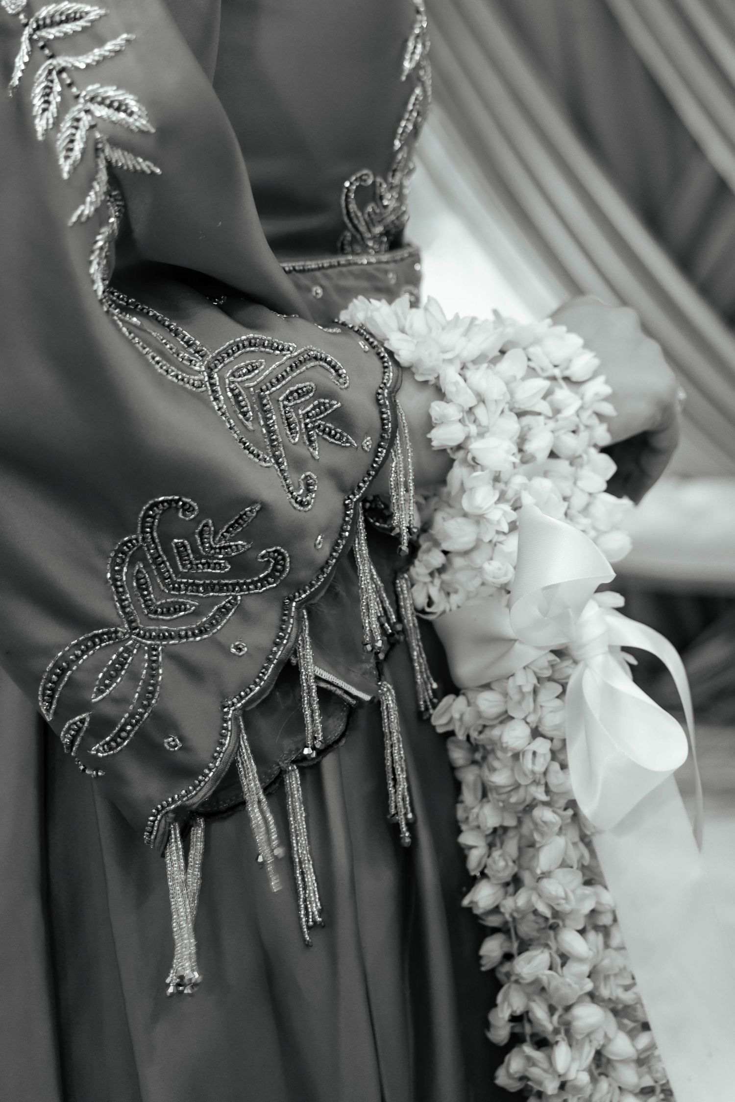 Close-up black and white detail of beaded formal dress with floral embroidery next to white flower bouquet.