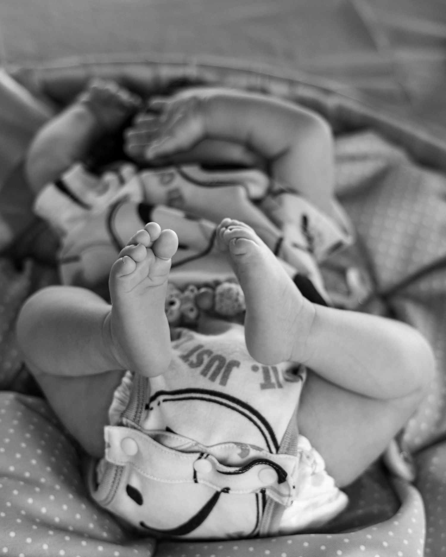 Close up black and white photo of tiny baby feet and hands against a soft blanket.