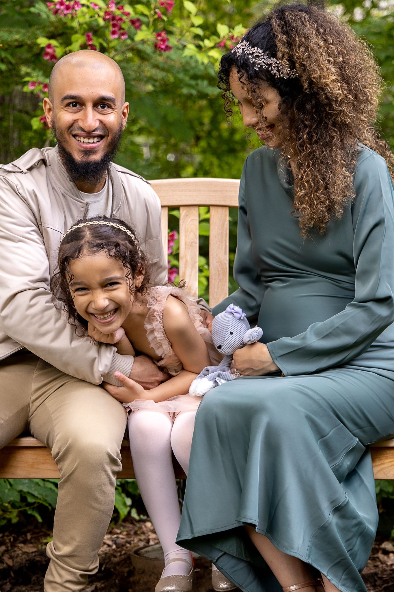 A family shares a joyful moment together while sitting on a wooden bench in a garden with blooming flowers.