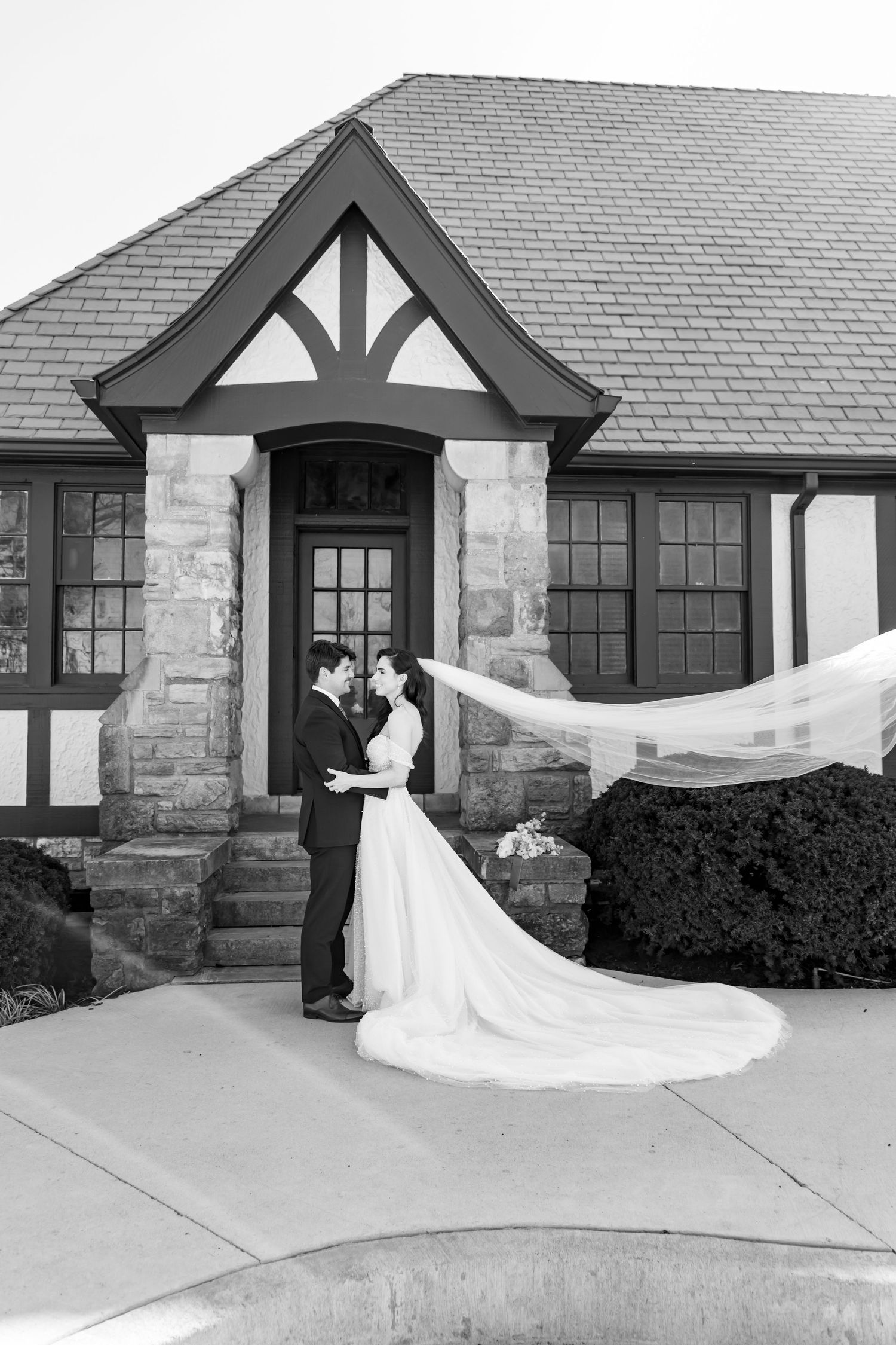 Black and white wedding portrait with flowing veil at Tudor-style entrance.