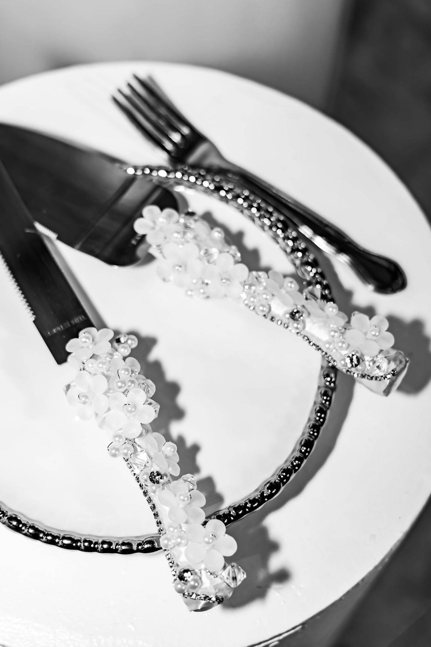Black and white photo of delicate beaded bridal hair accessories and utensils on a white plate.