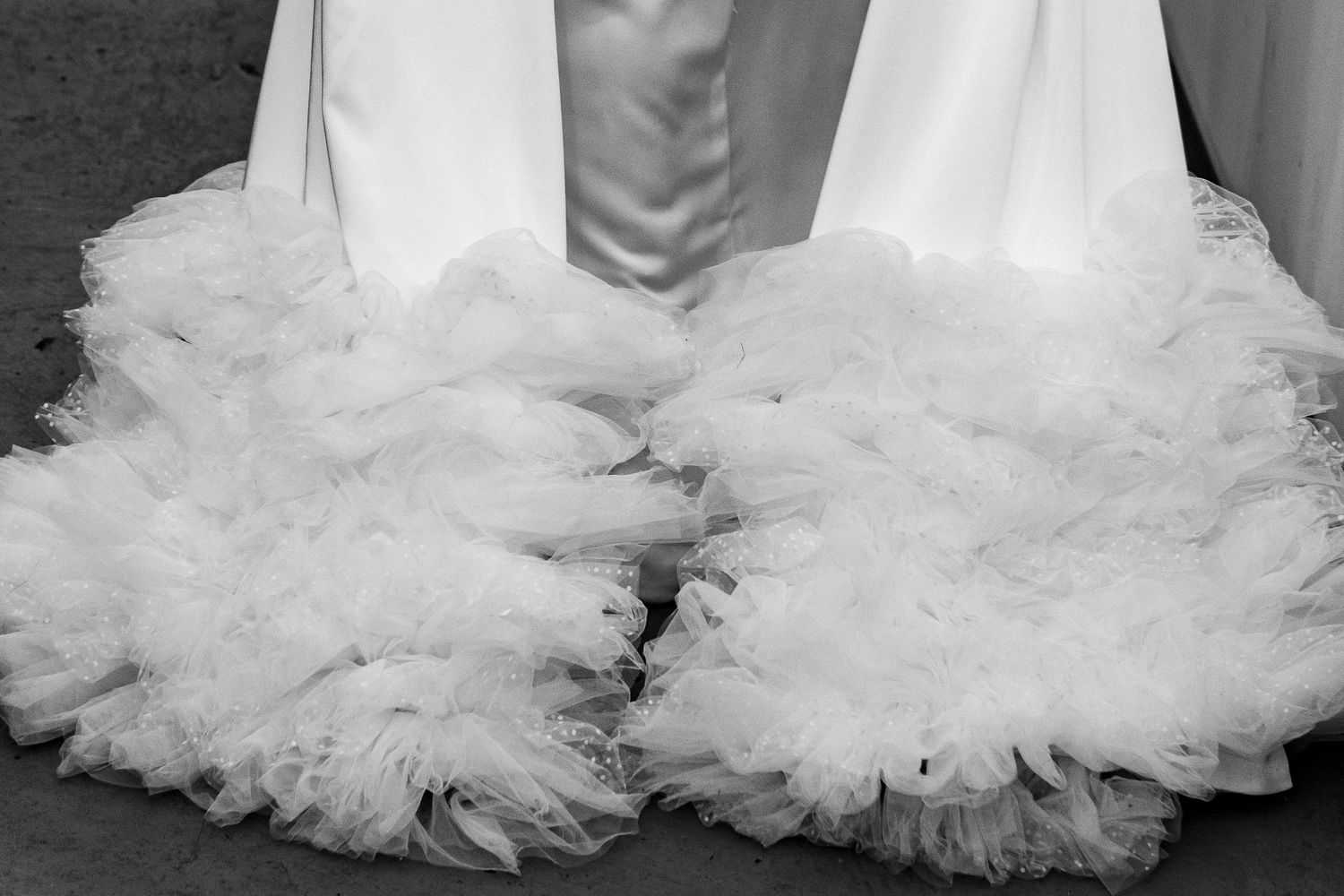 Black and white photograph showing the bottom ruffled layers of a white wedding dress with tulle fabric.