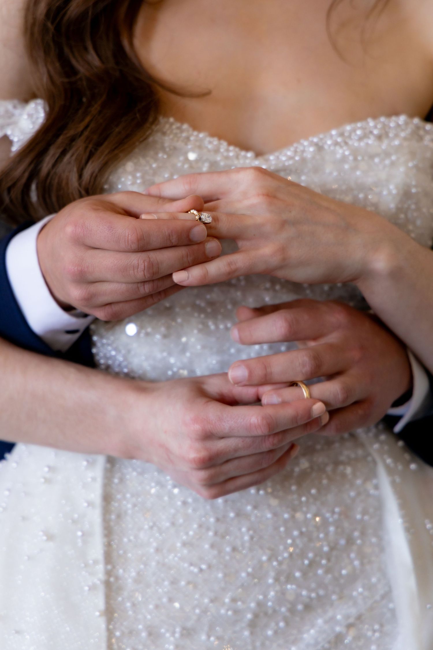 Close-up of hands exchanging rings on sparkly wedding dress.