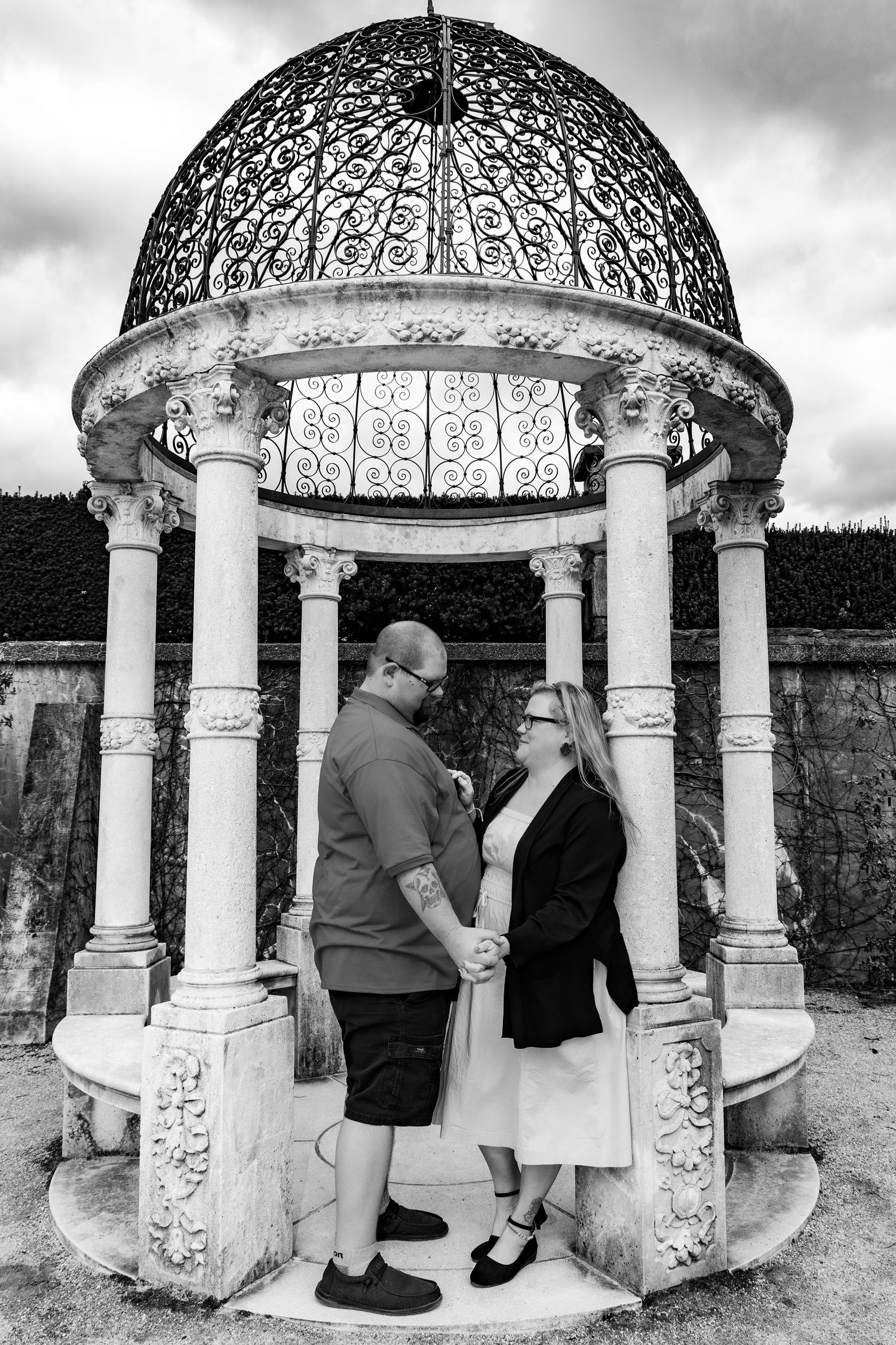 Ornate stone gazebo with decorative dome and columns in a garden setting.