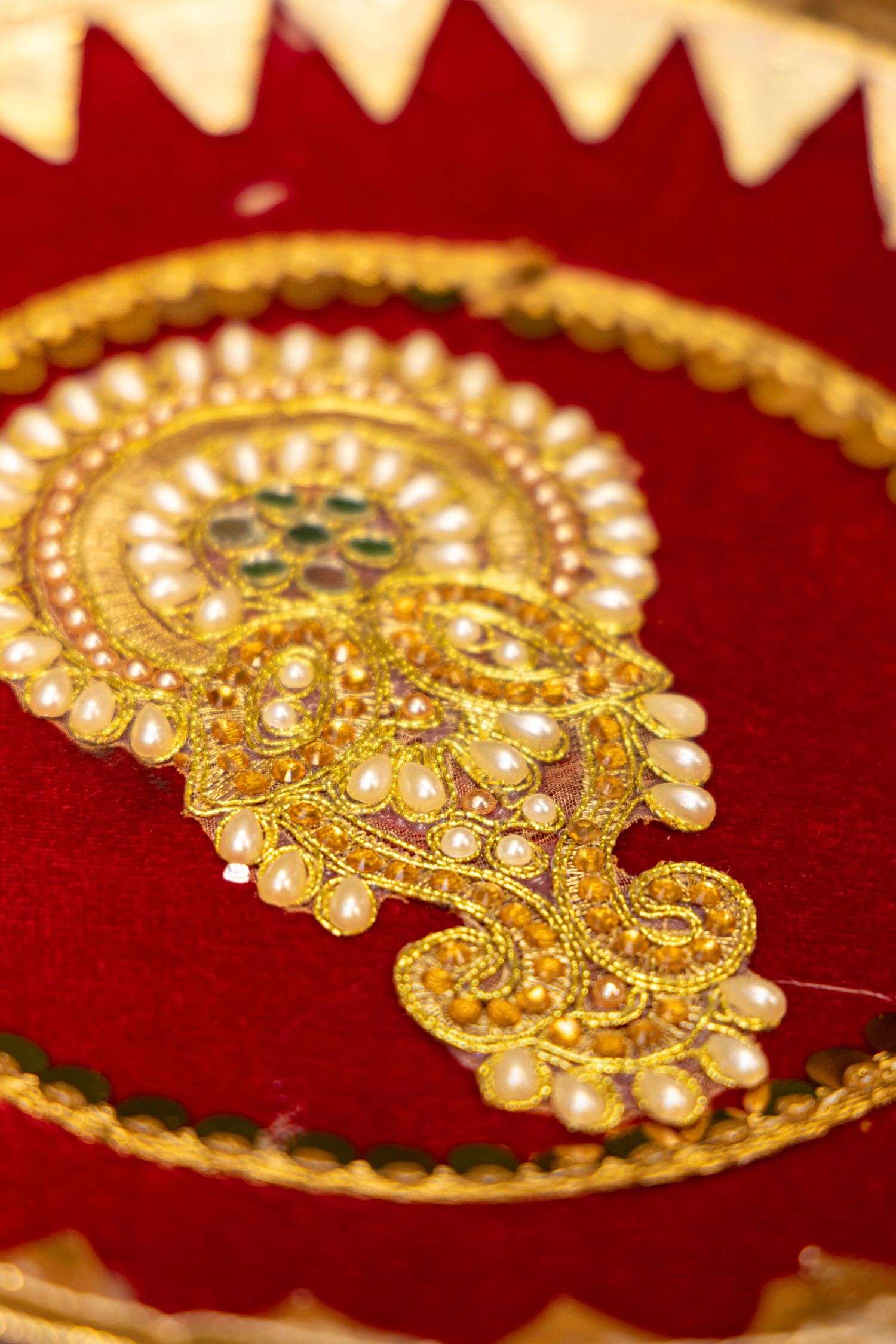 Ornate golden Indian jewelry piece with pearls and intricate designs displayed on red velvet background.