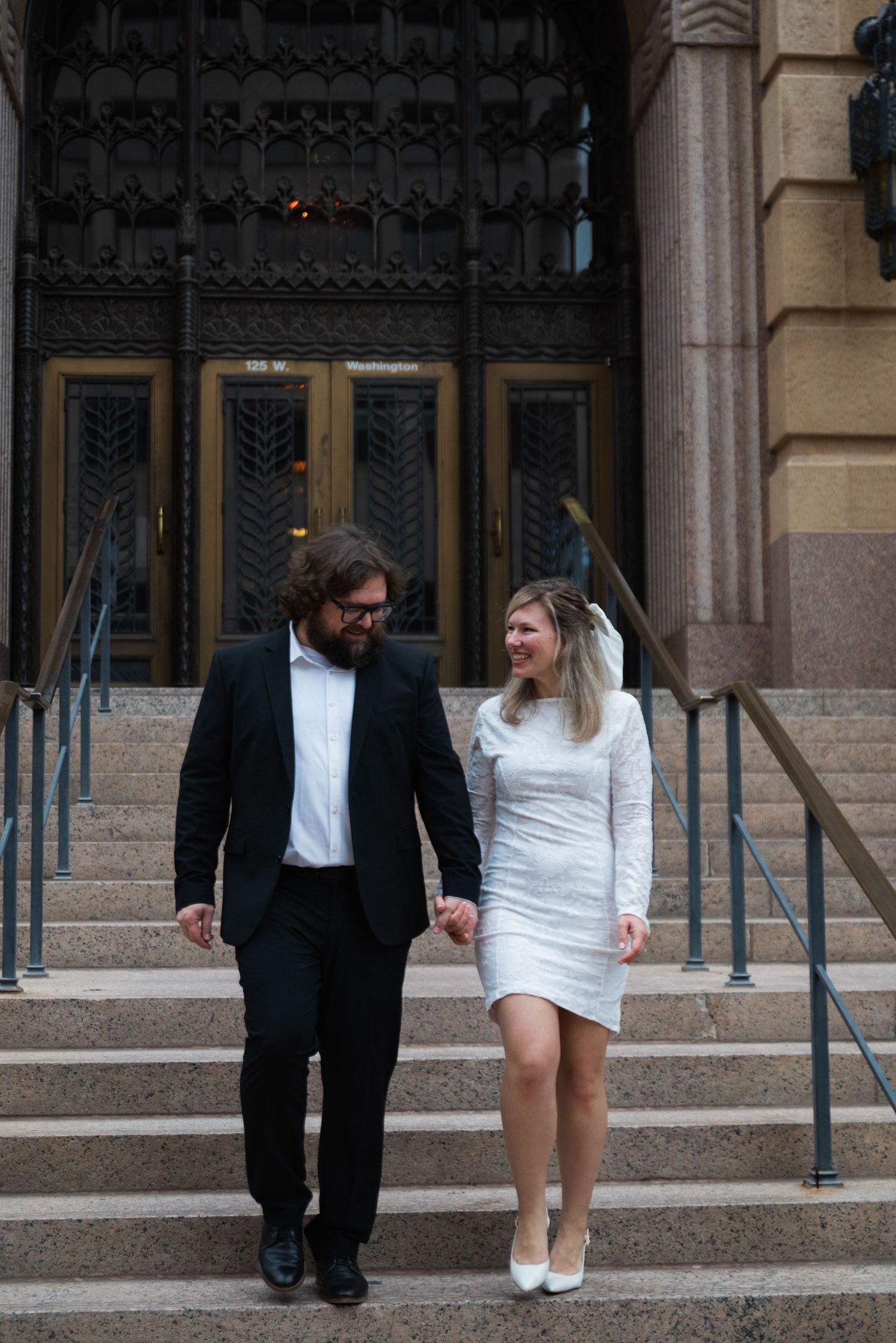 A couple playfully posing on stone steps outside a historic building with ornate architecture.