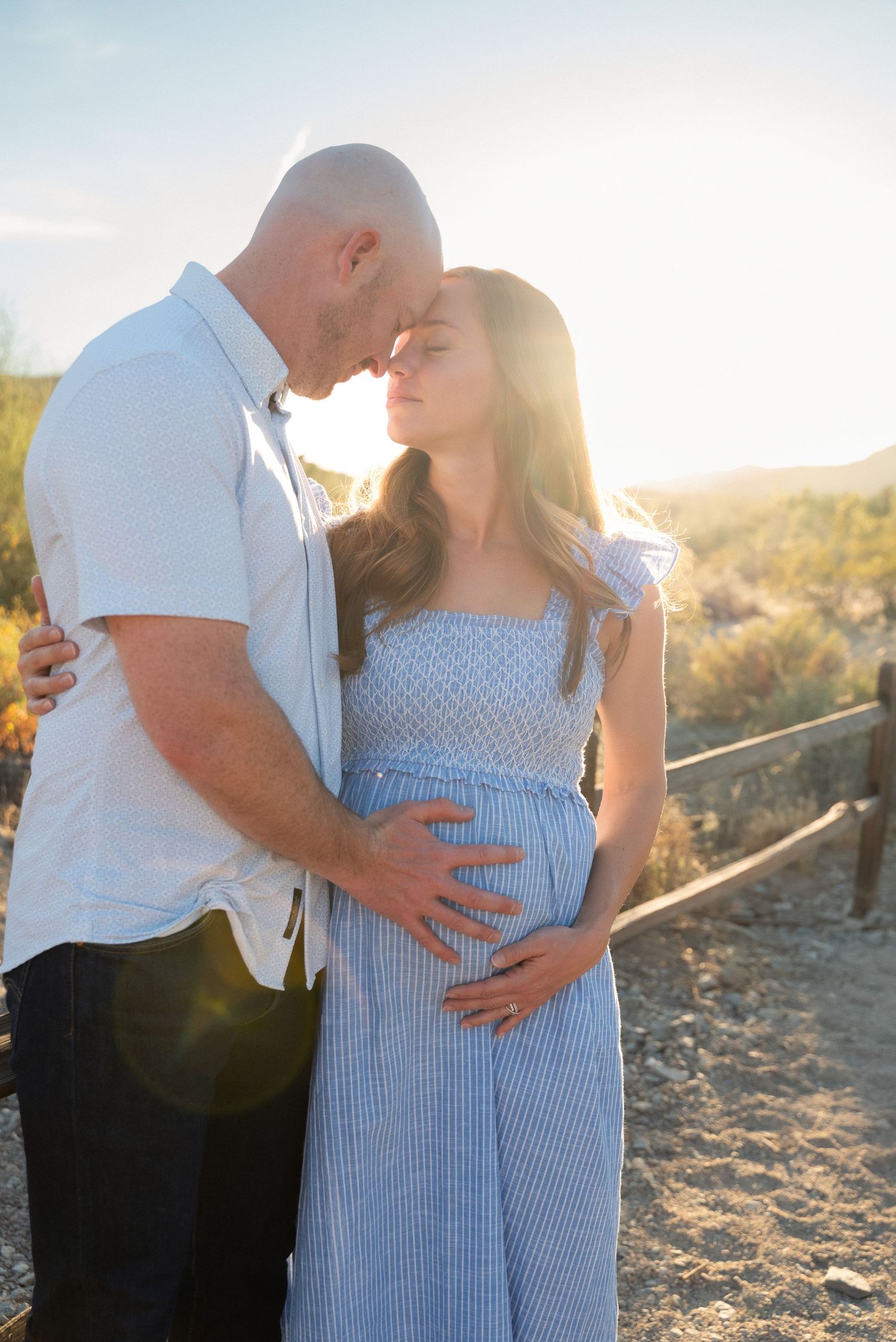 Maternity photoshoot in desert landscape at sunset with couple embracing in soft golden light.