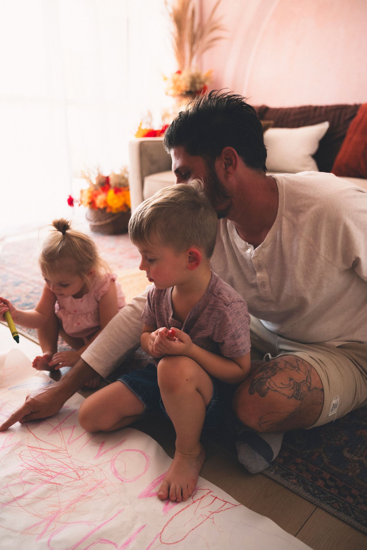 Family members lying down on the floor together and drawing on a large piece of paper spread out before them.