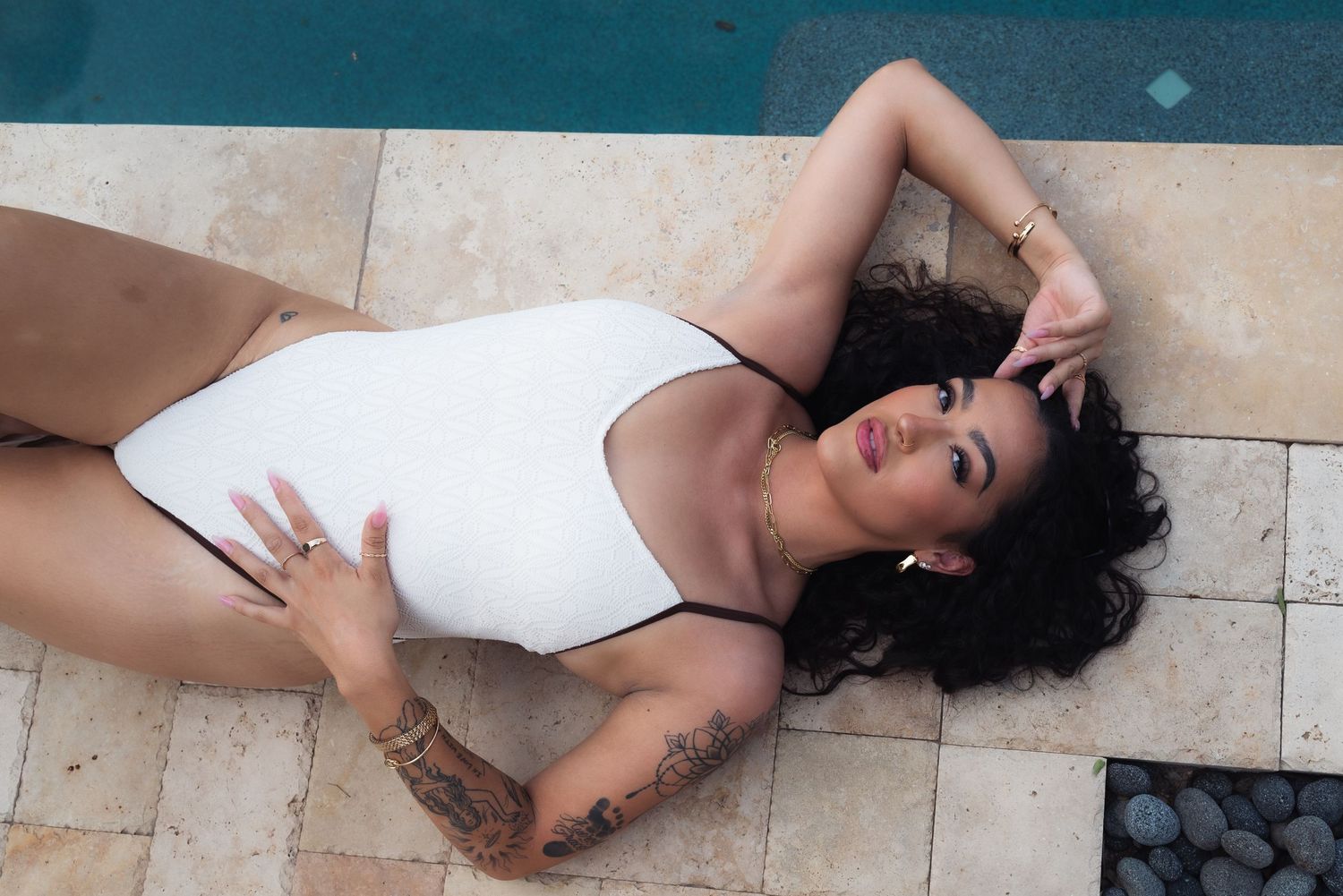 A person in a white outfit lies on a beige tiled floor in a dramatic pose.