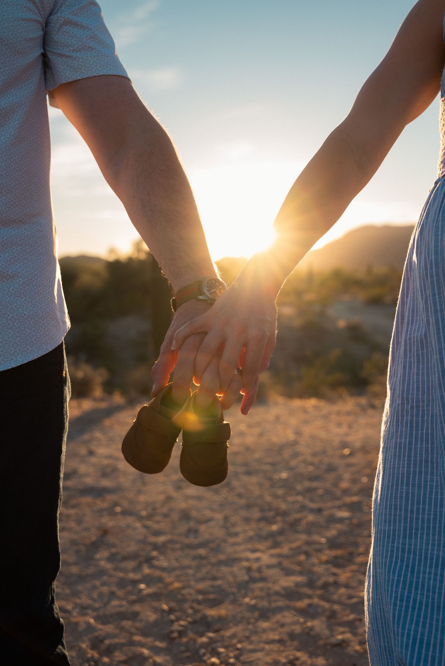 Two people holding hands silhouetted against a warm sunset sky over a desert landscape.