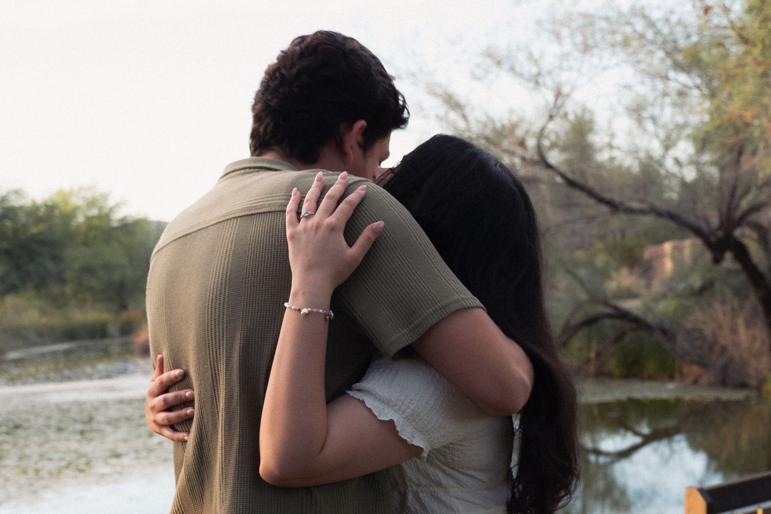 A couple embraces in an intimate moment outdoors with trees and natural scenery in the background.
