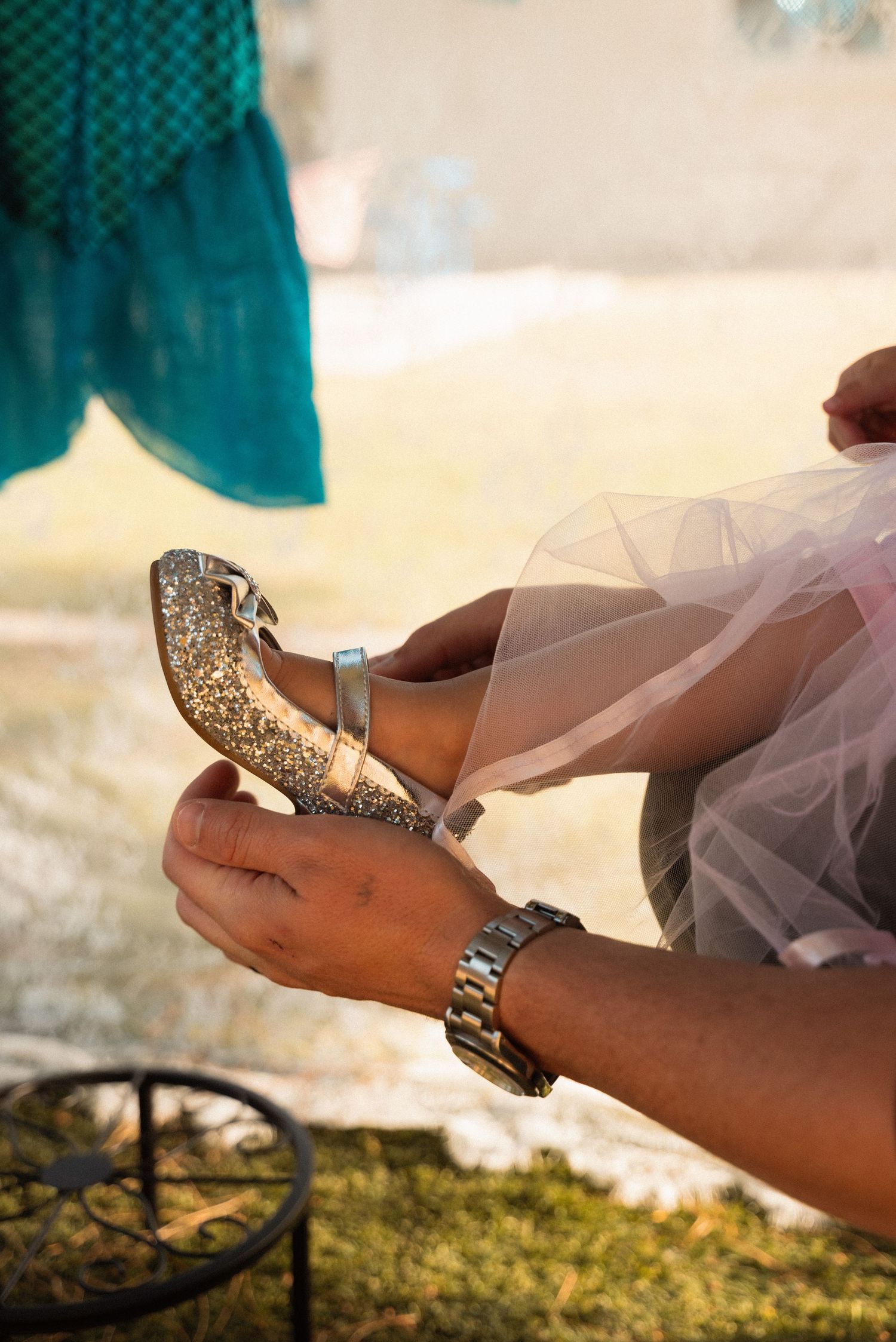 Person fastening a glittery gold high heel shoe on a woman wearing a pink tulle dress outdoors.