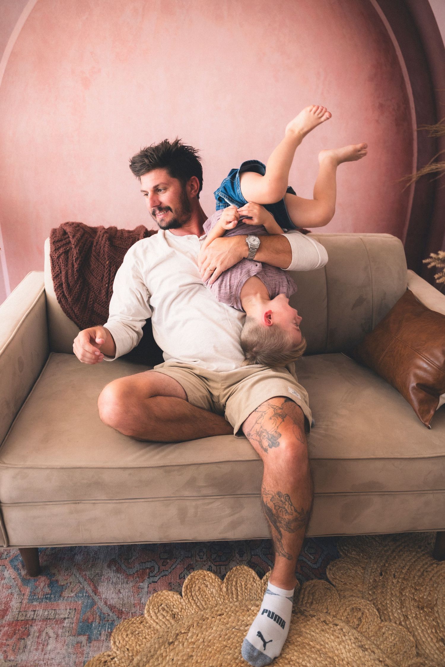 A playful moment on a beige couch shows parent and child having fun and being silly together.