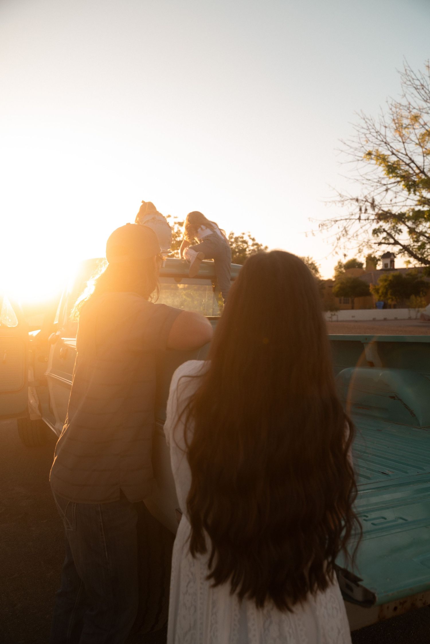 Couple silhouetted against vibrant sunset glow watching children play near a pool outdoors.