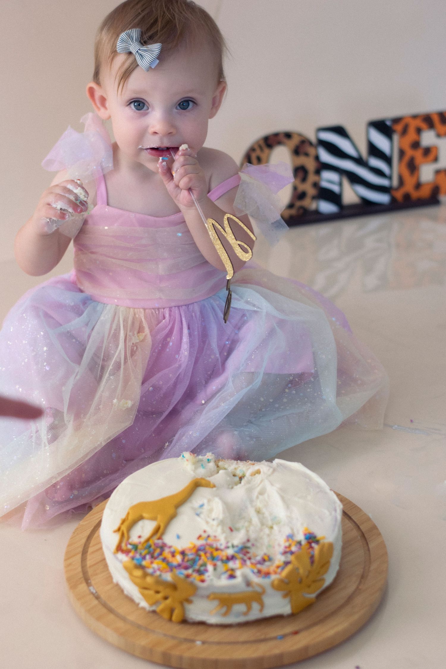 A colorful birthday cake with rainbow sprinkles and gold decorations sits on a wooden serving board.