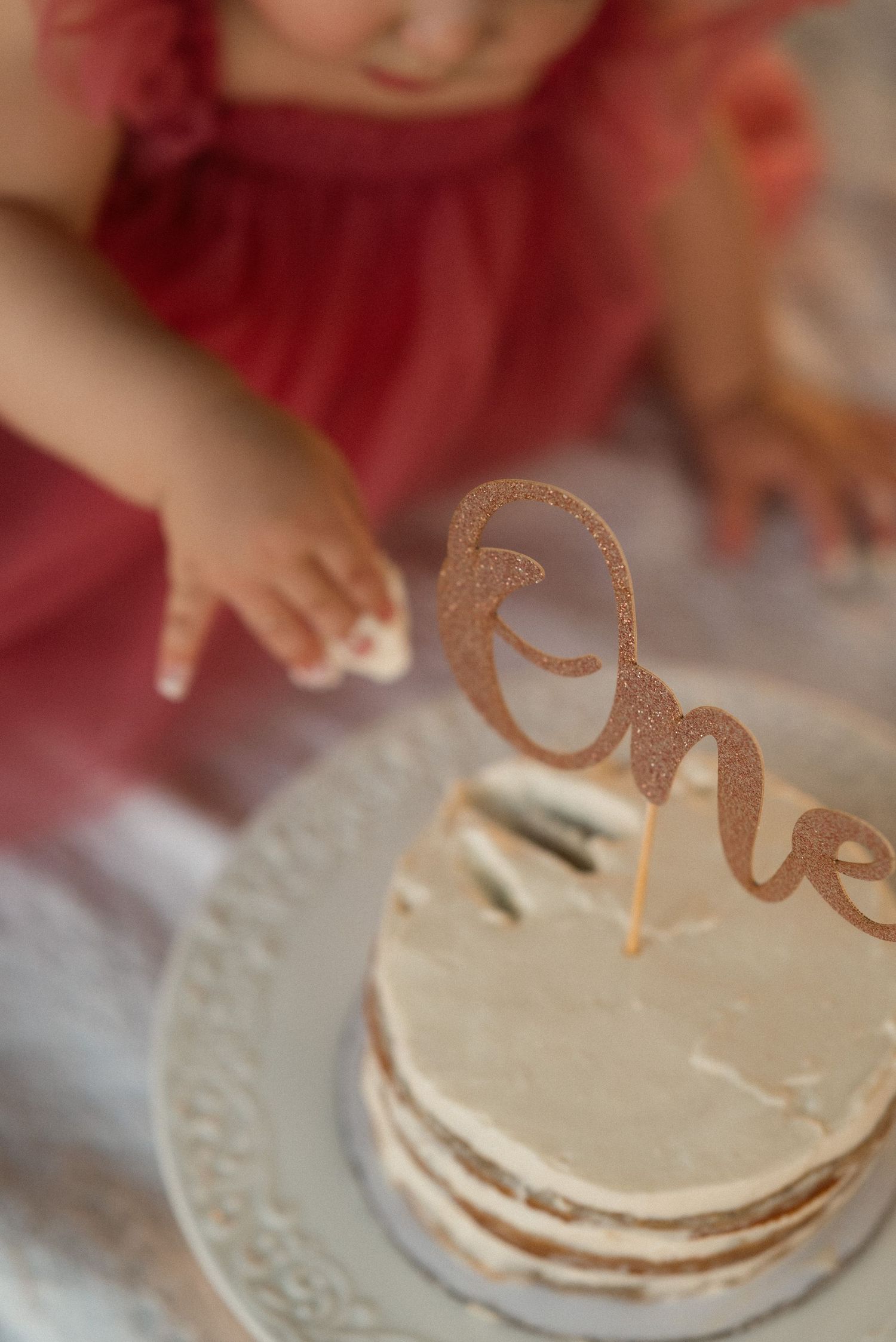 Baby girl in red dress reaching for a white smash cake with a rose gold glitter 