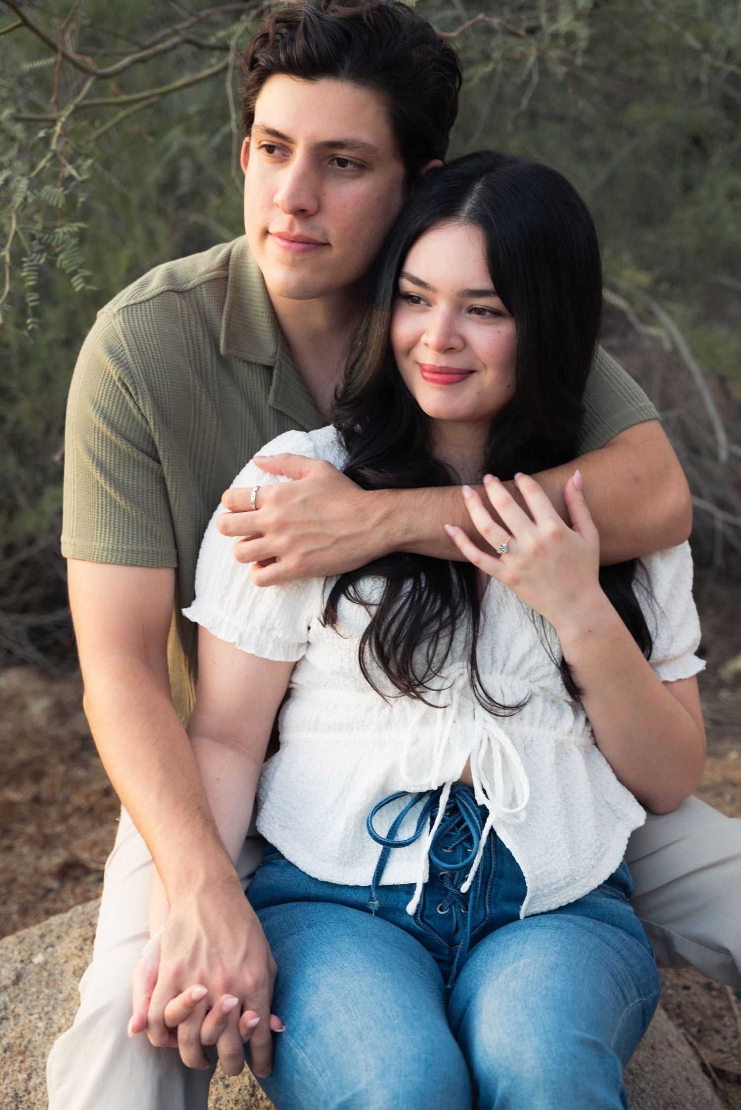 A couple shares an intimate moment outdoors, with her wearing a white top and blue jeans.