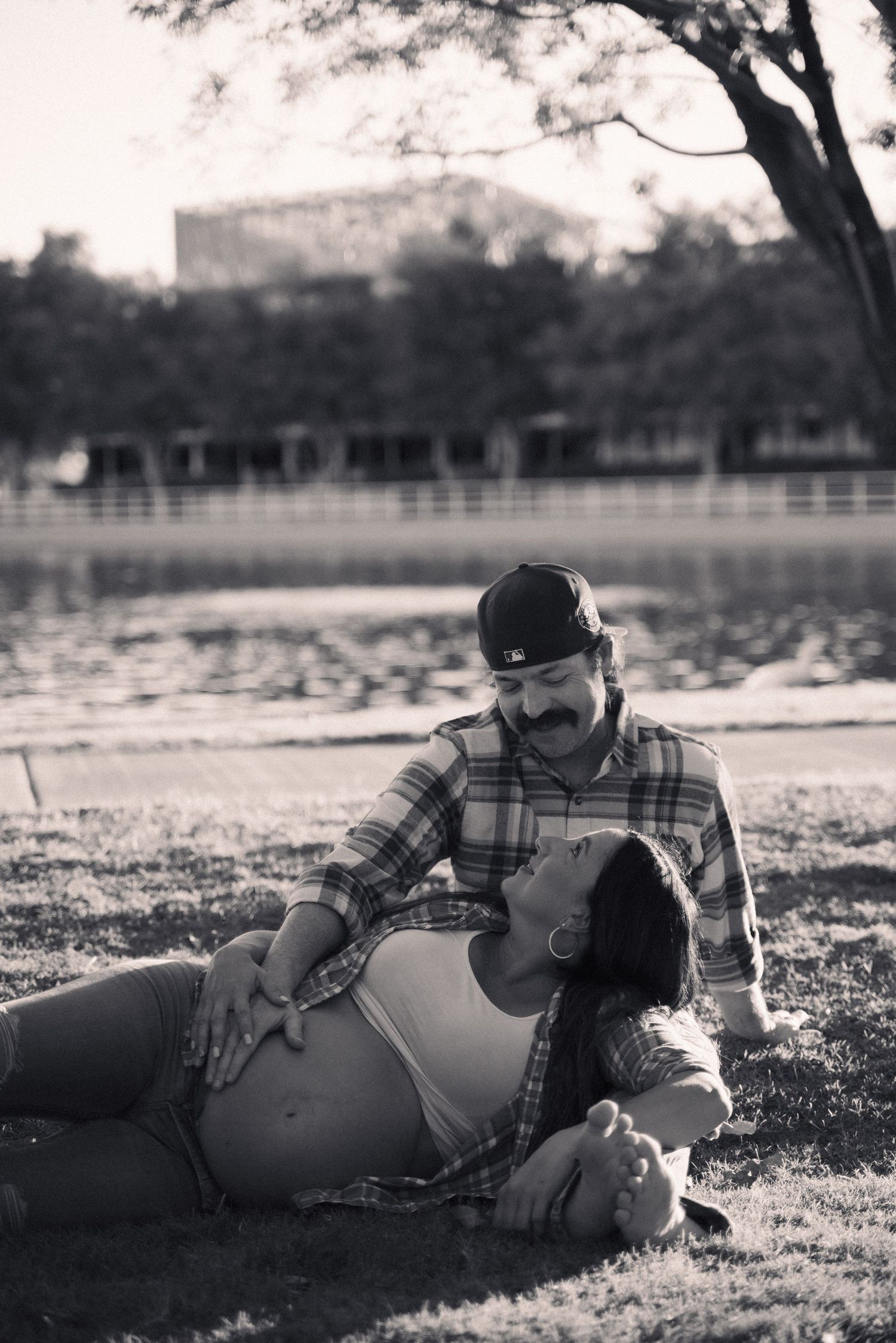 A couple shares an intimate black and white moment by a lake during their maternity photoshoot.