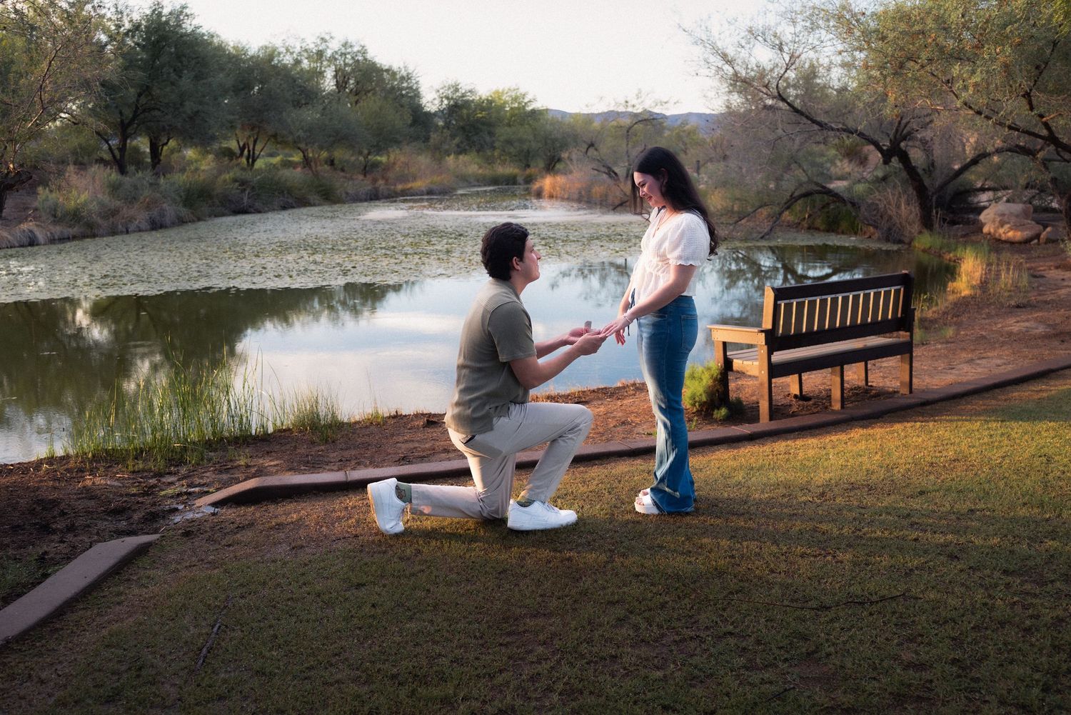 People sitting on a park bench overlooking a serene lake during sunset.