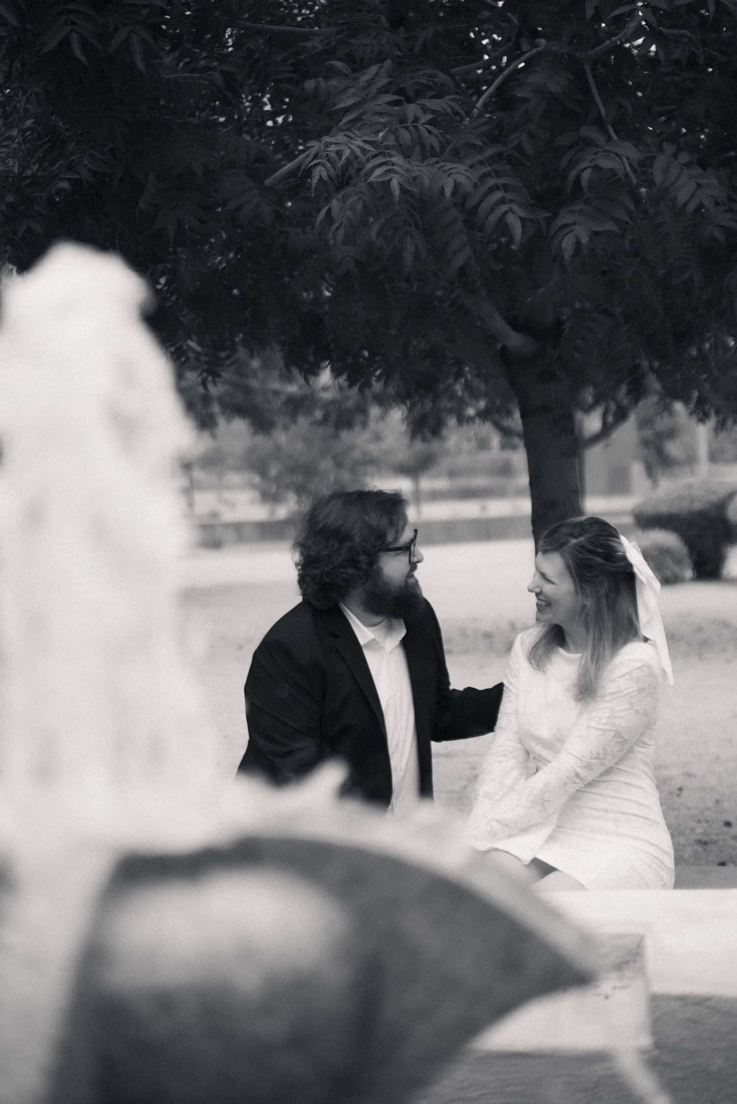 A black and white photo shows two people sitting together in a dreamy outdoor garden setting.