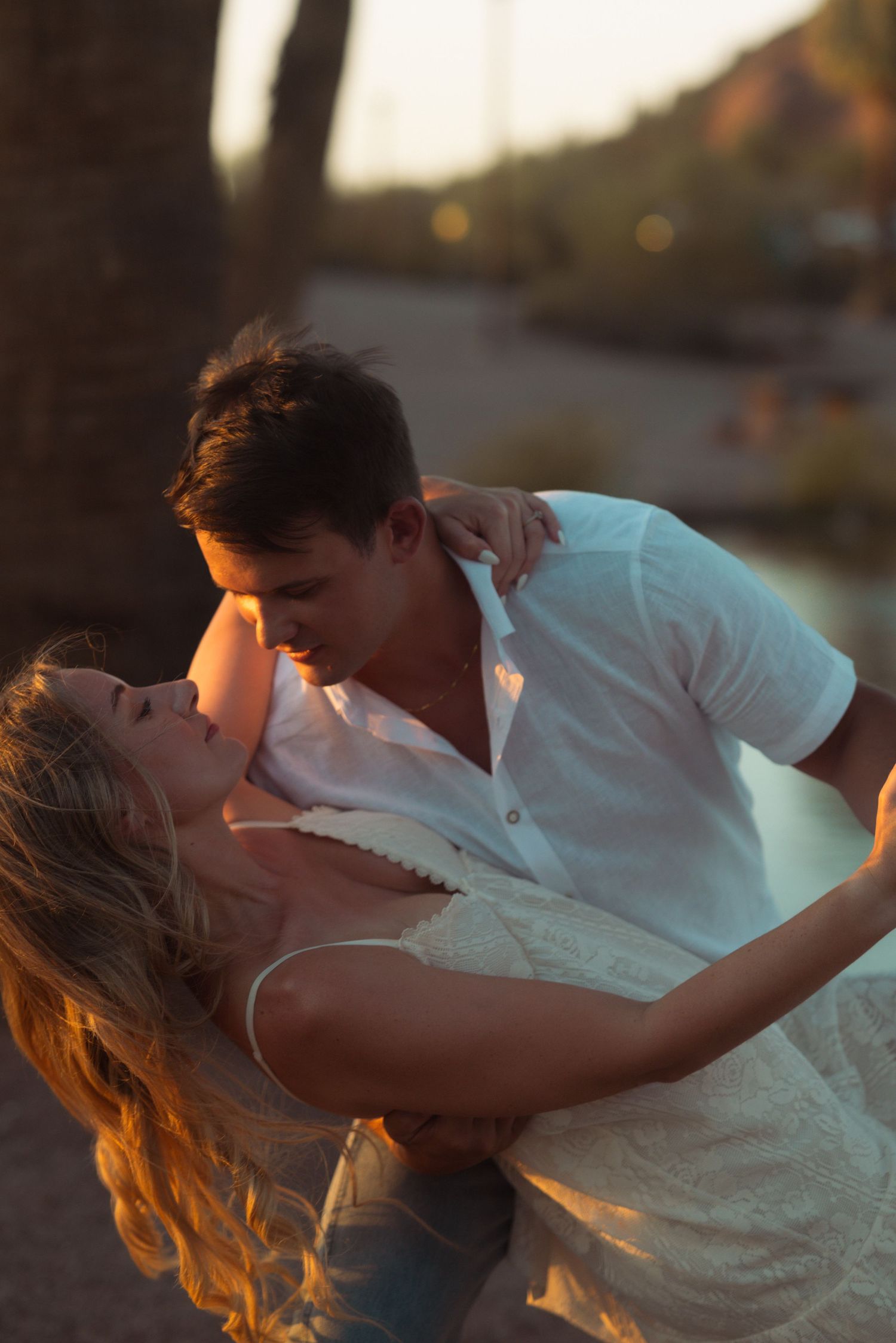 Romantic couple sharing a tender kiss at golden hour sunset, man in white shirt dipping woman with blonde hair.