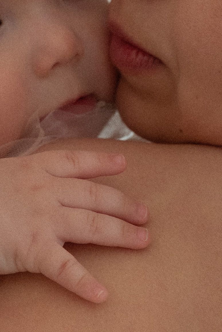 Close-up of a mother kissing her newborn baby, with the infant's tiny hand resting gently on her shoulder.