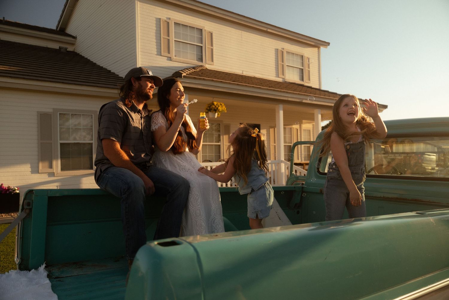 Family enjoying a sunny evening together on a vintage teal truck bed outside a charming suburban home.