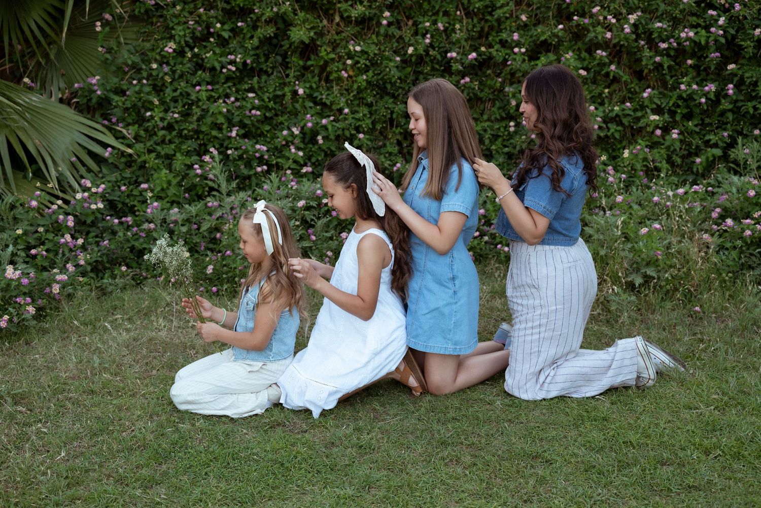 Three people kneeling in garden pose together wearing light blue and white casual outfits.