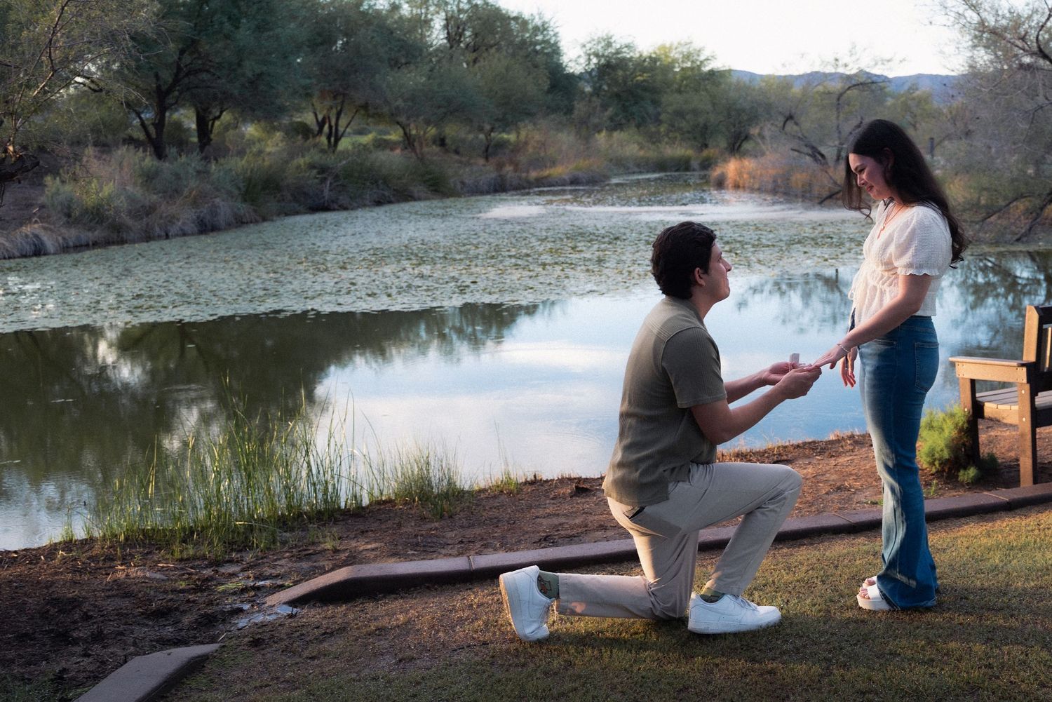 Two people sit together on a blanket by a serene lake during sunset, enjoying a peaceful outdoor moment.