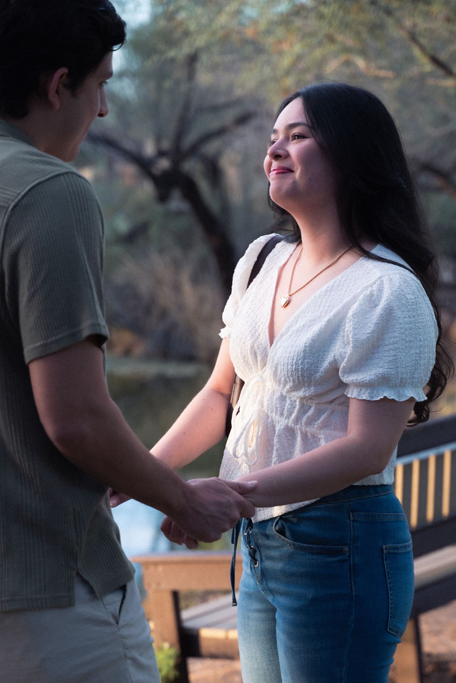 Close up view of two people holding hands outdoors during sunset with a wooden bench in the background.