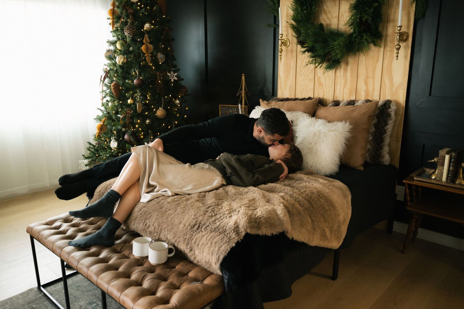 A cozy winter living room decorated with a wreath, fur throws, and dark painted walls creates an elegant atmosphere.