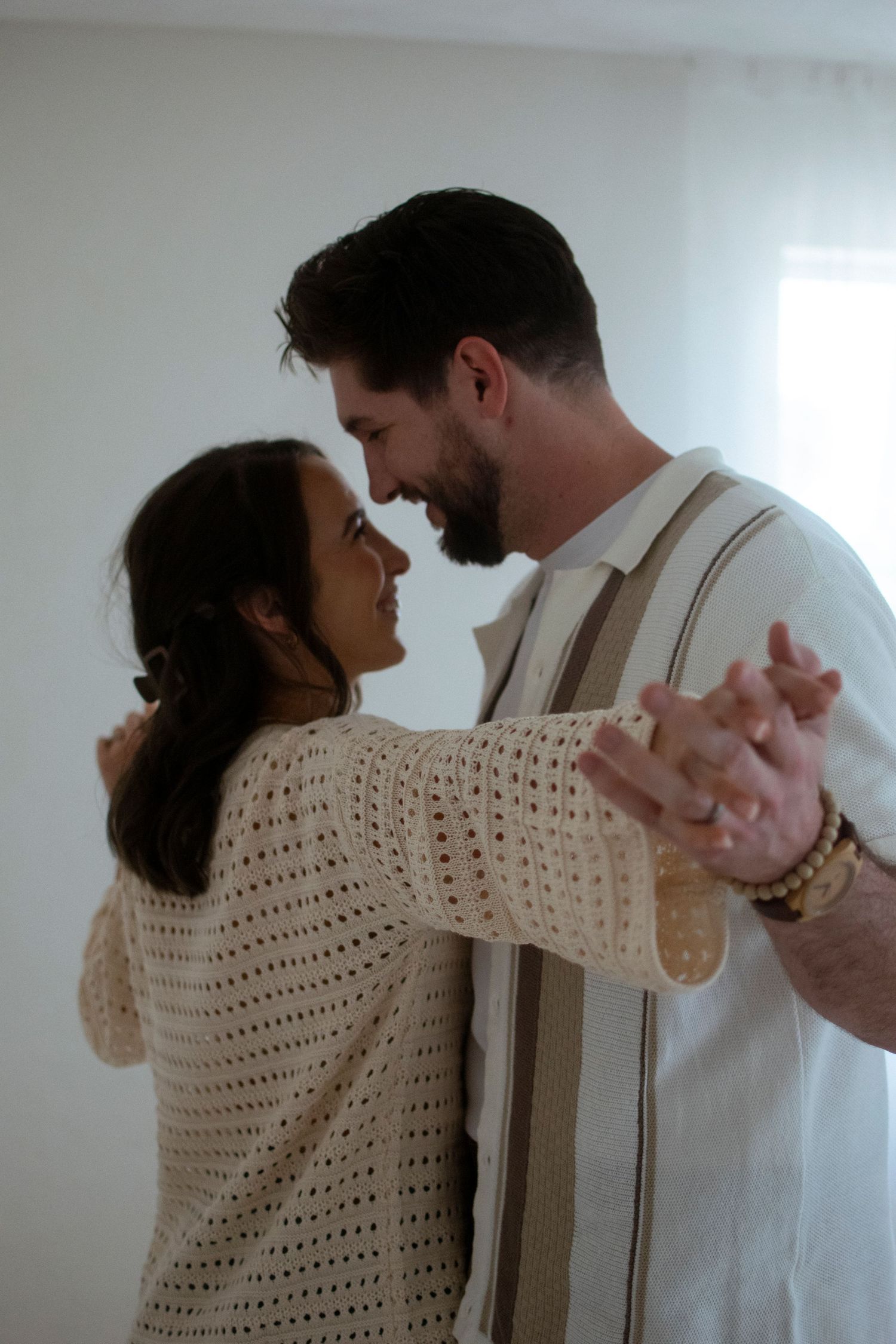 A couple in casual attire dance together in a sequence of romantic moves against a white wall backdrop.