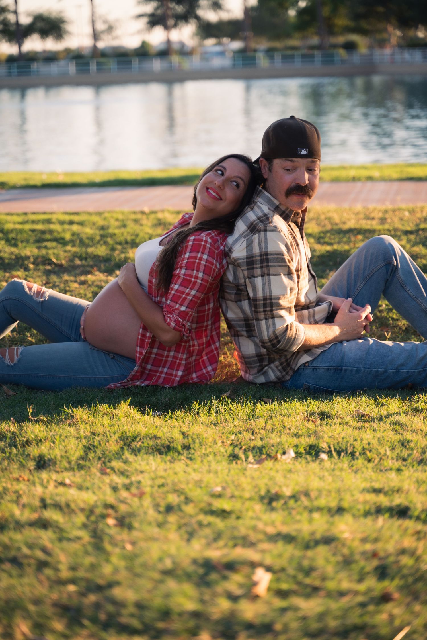 A couple relaxes together on grassy lawn during golden hour sunset by a lake.