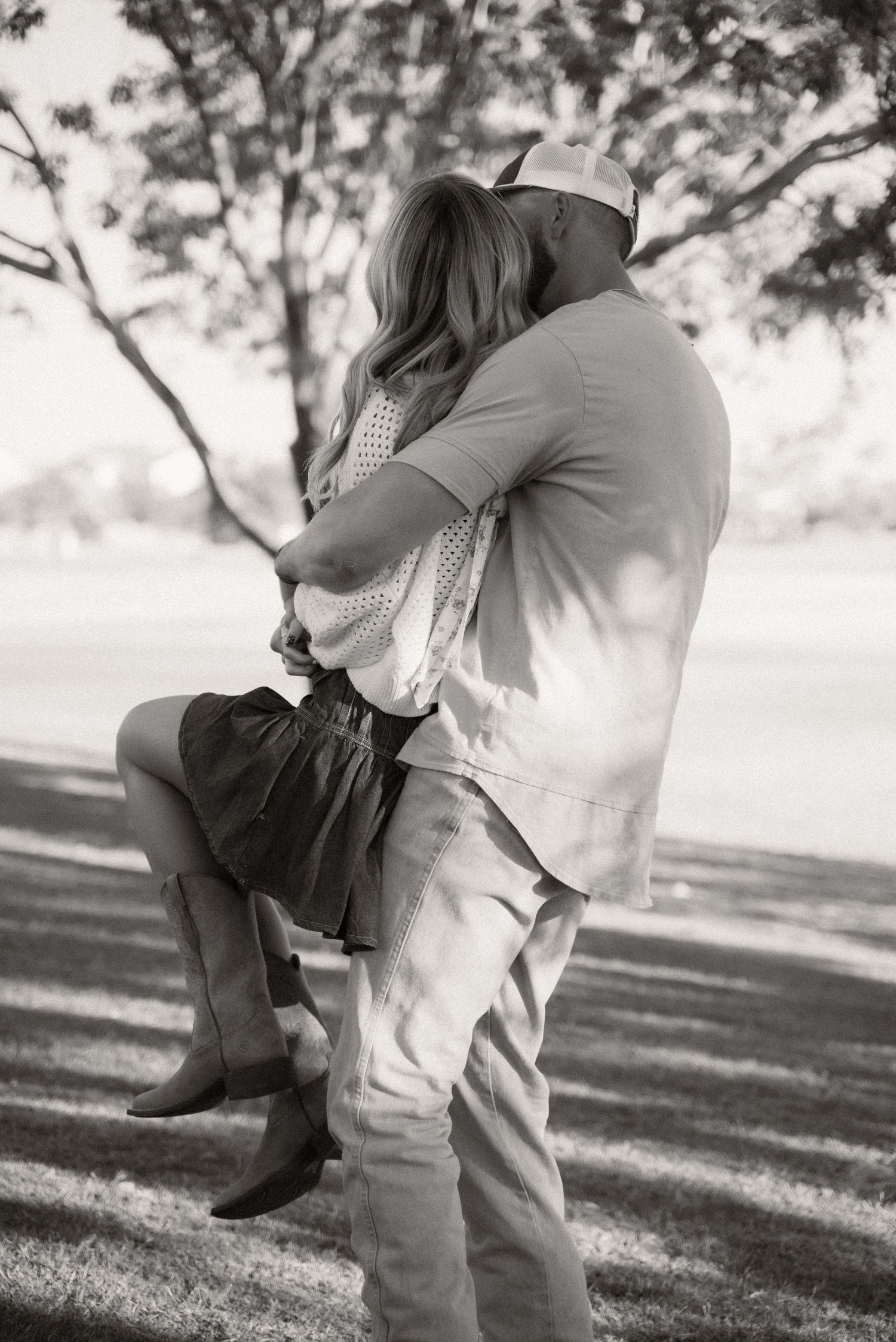 A black and white photo captures an intimate embrace between a couple in a park setting.