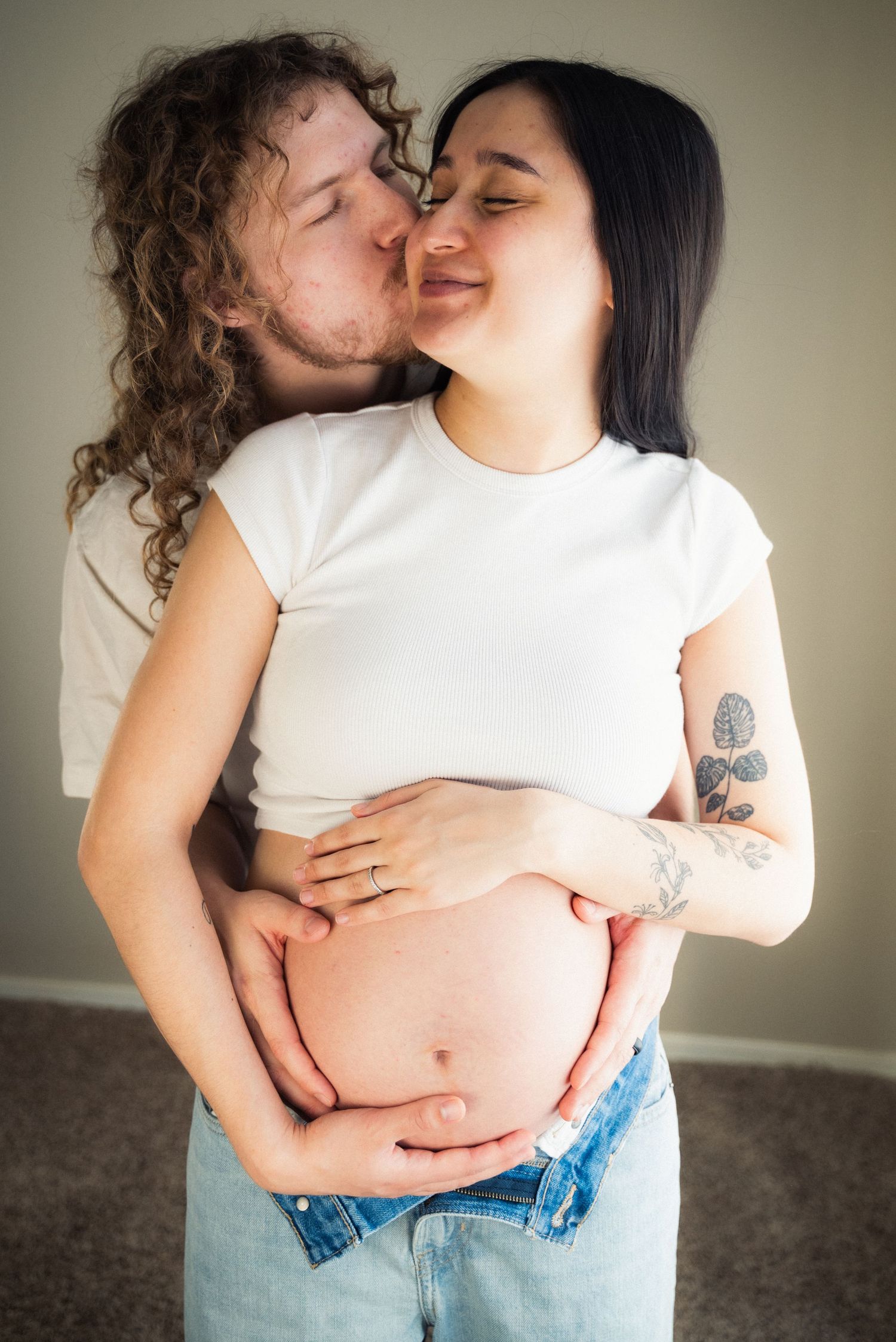 An intimate maternity photoshoot featuring a couple in white shirts and jeans showing affection.