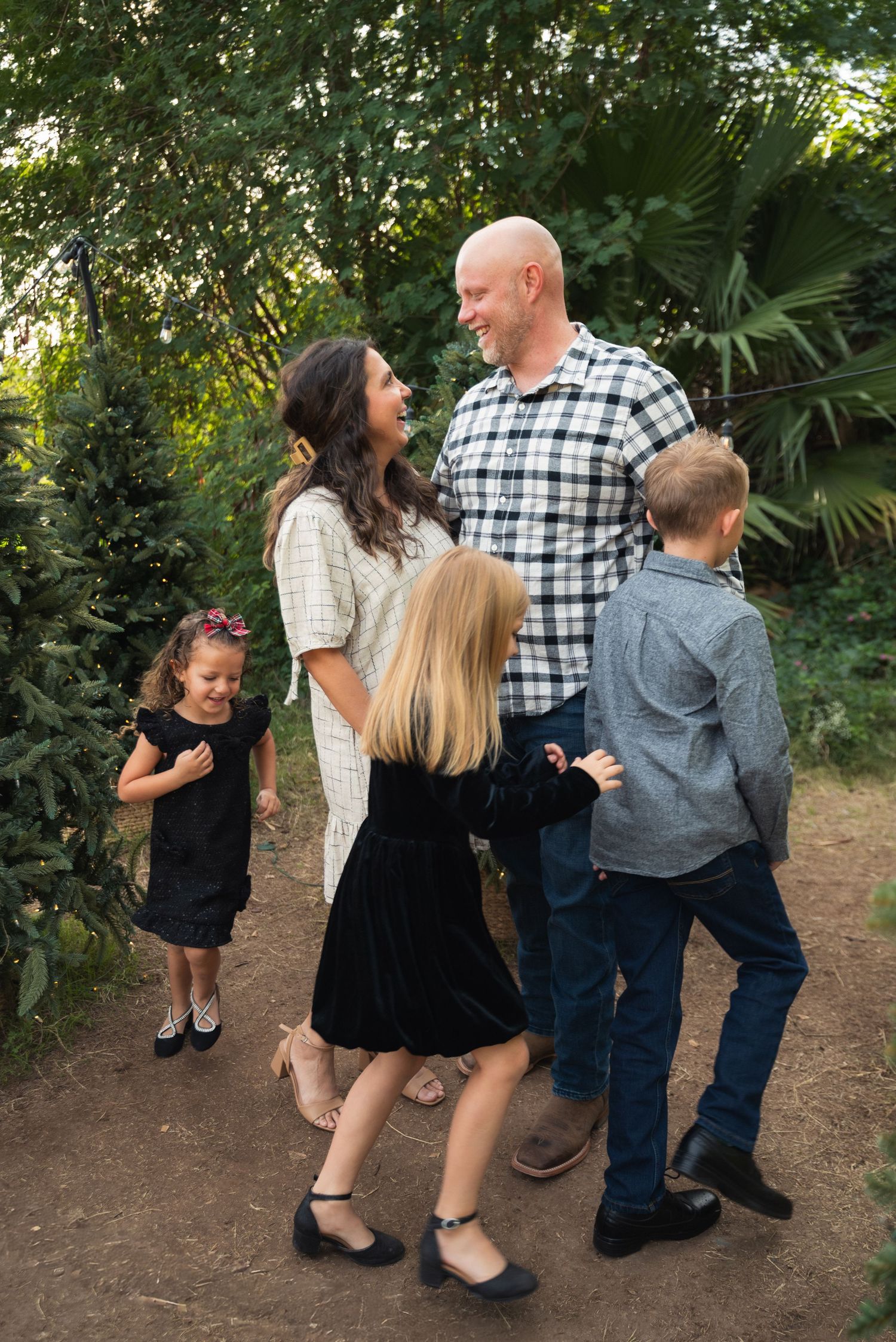 Family of five laughing together on a garden path, parents and three children dressed in black and plaid outfits.