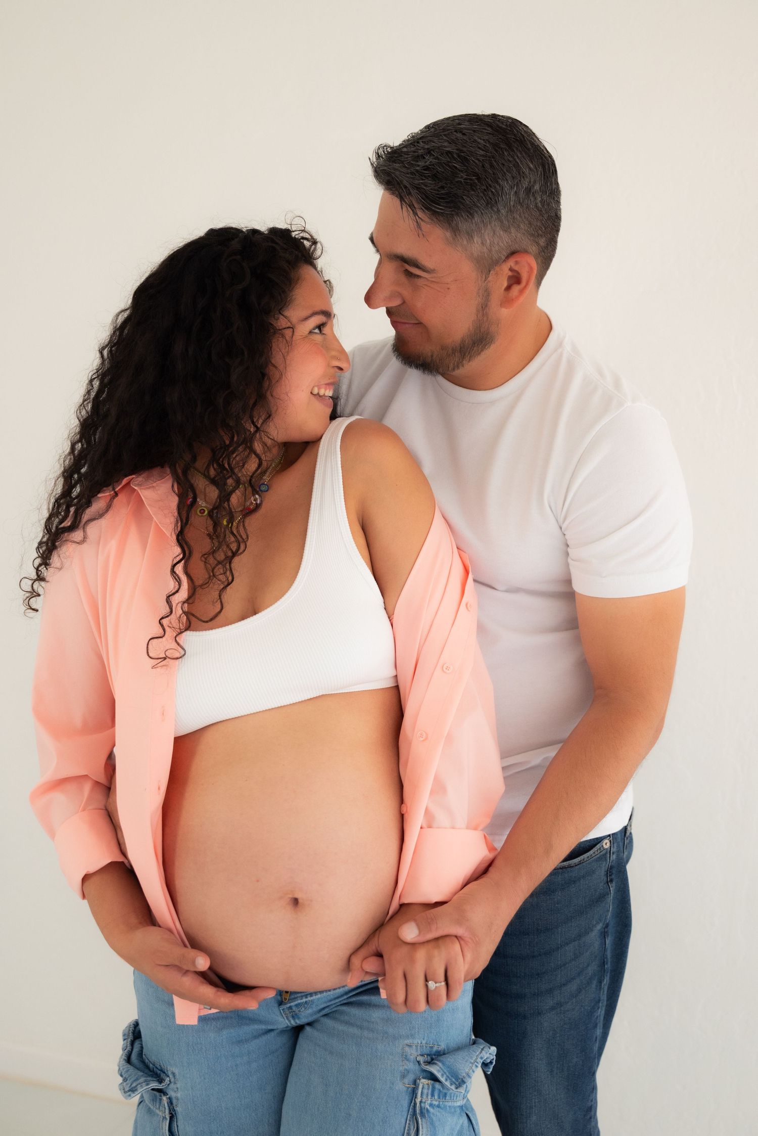 Couple in white and peach tops sharing tender pregnancy moments in a progressive photo series against white background.