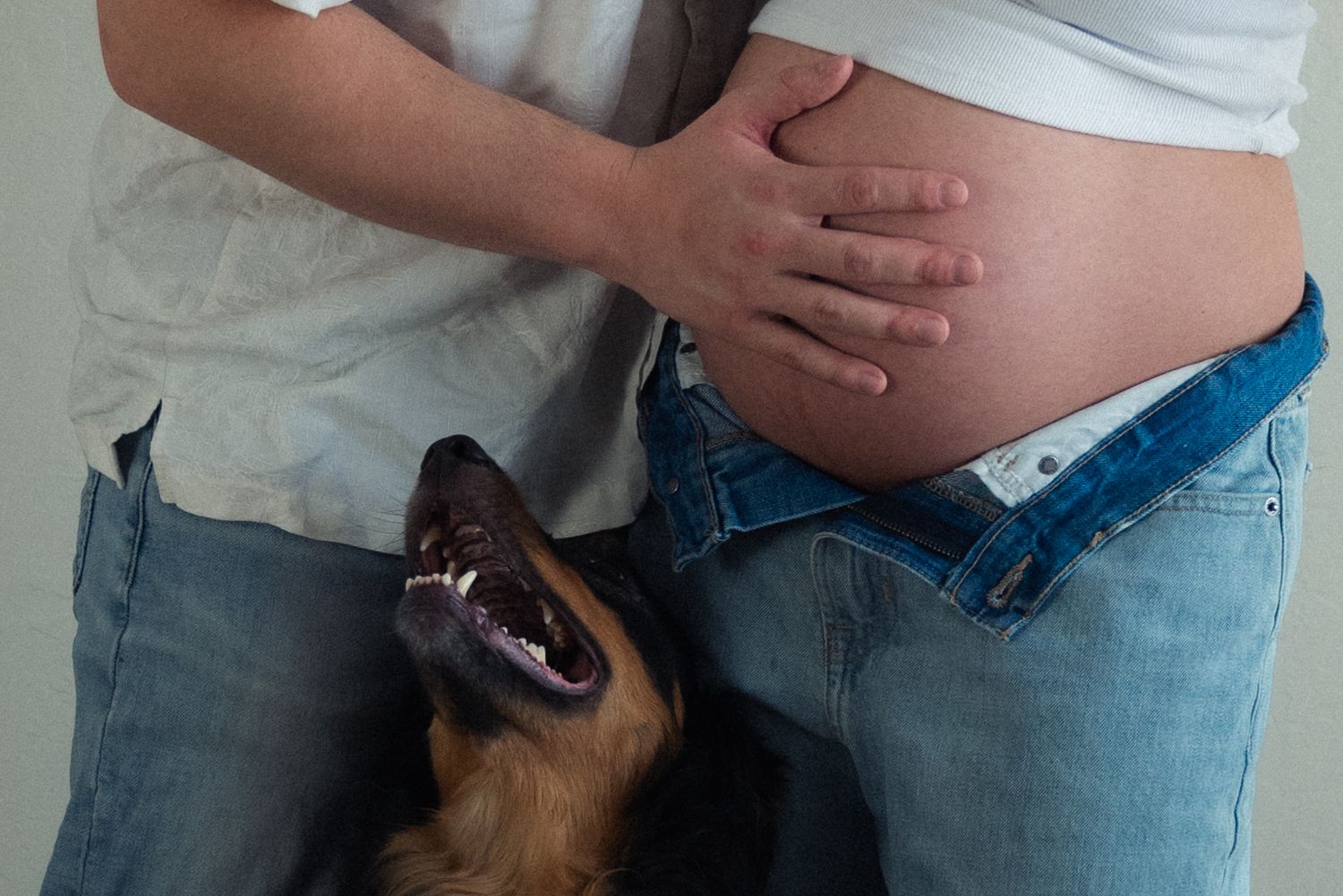 A small brown dog moves away from a line of standing people wearing blue jeans and white shirts.