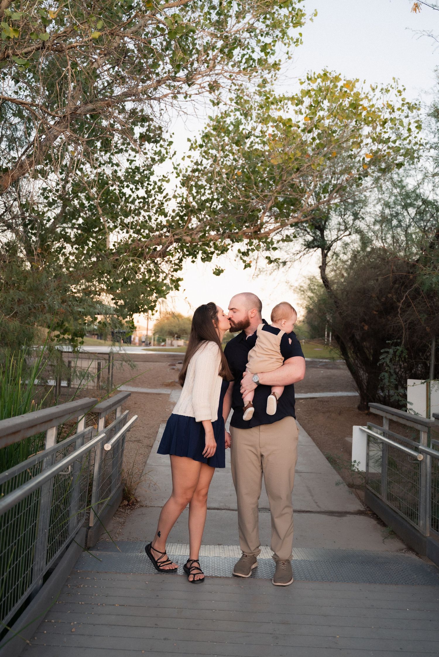 A family shares an intimate moment together on a wooden bridge pathway during sunset.