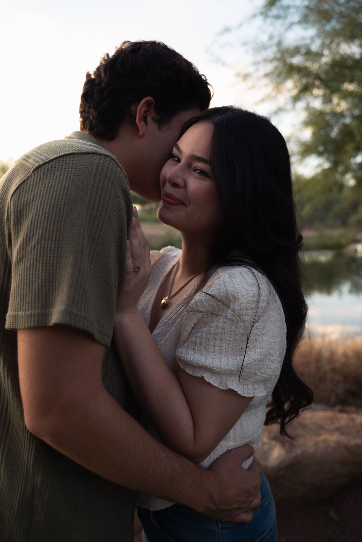 A romantic couple embraces in silhouette against a natural outdoor setting at dusk.