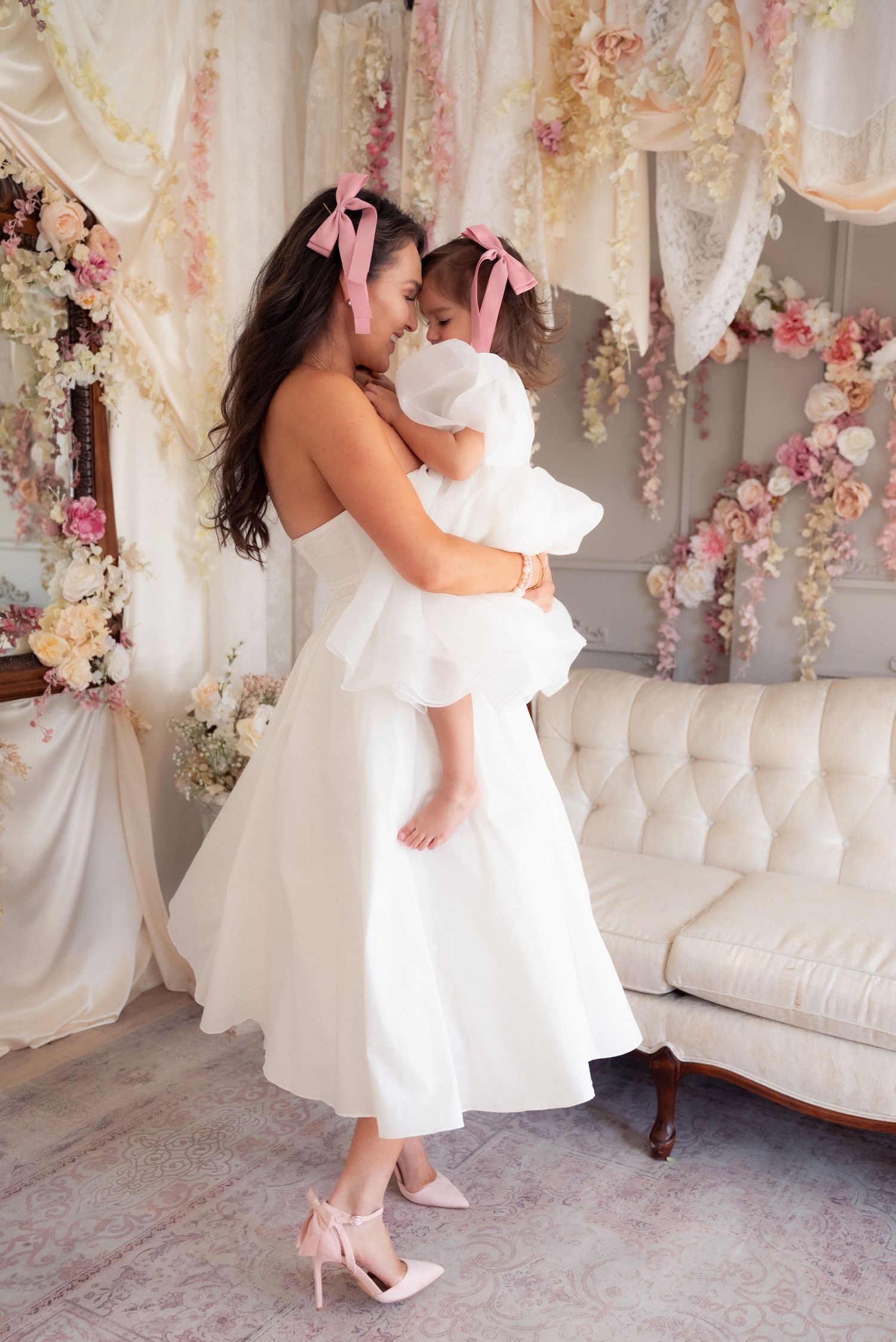 Mother and daughter in matching white dresses dance together in an elegant pink floral decorated room.