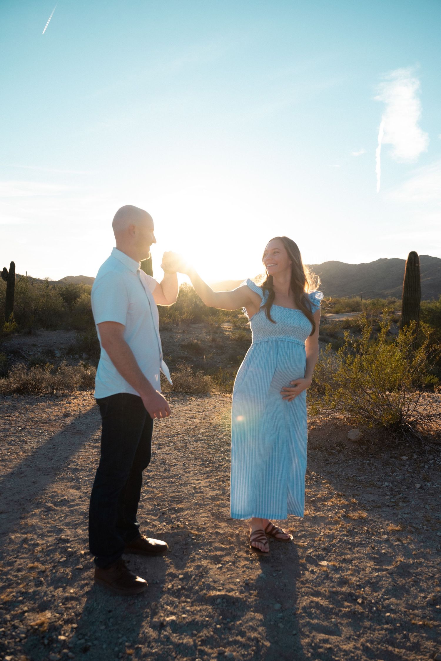 Desert maternity photo with expectant couple standing together against mountain backdrop at golden hour.