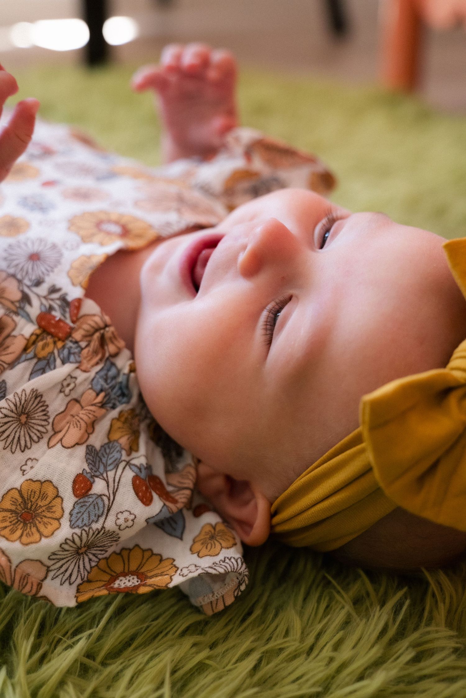 Side view portraits of an infant in floral patterned clothing resting on green carpet.