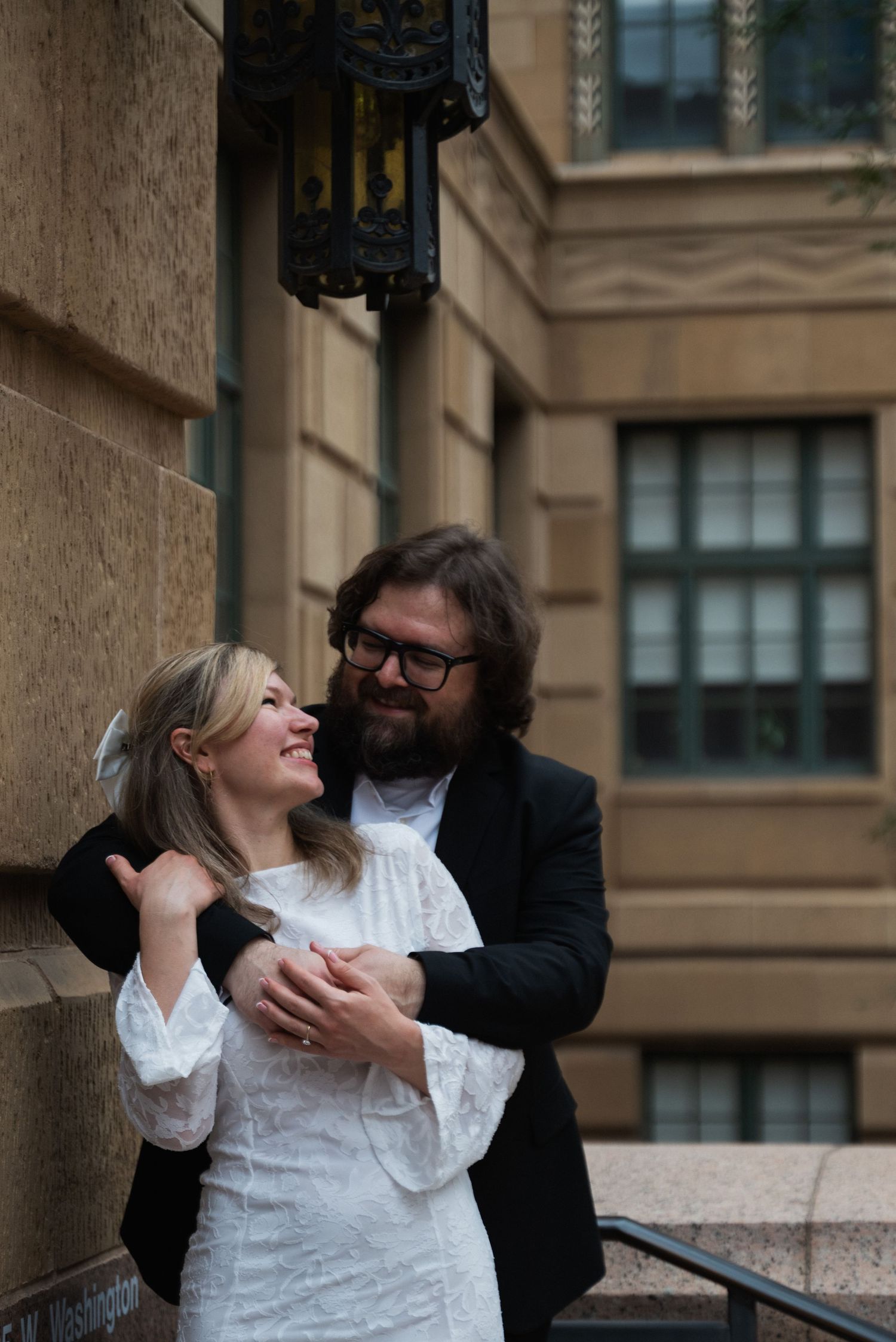 Romantic couple in formal wear share intimate moments while posing against an urban building exterior.