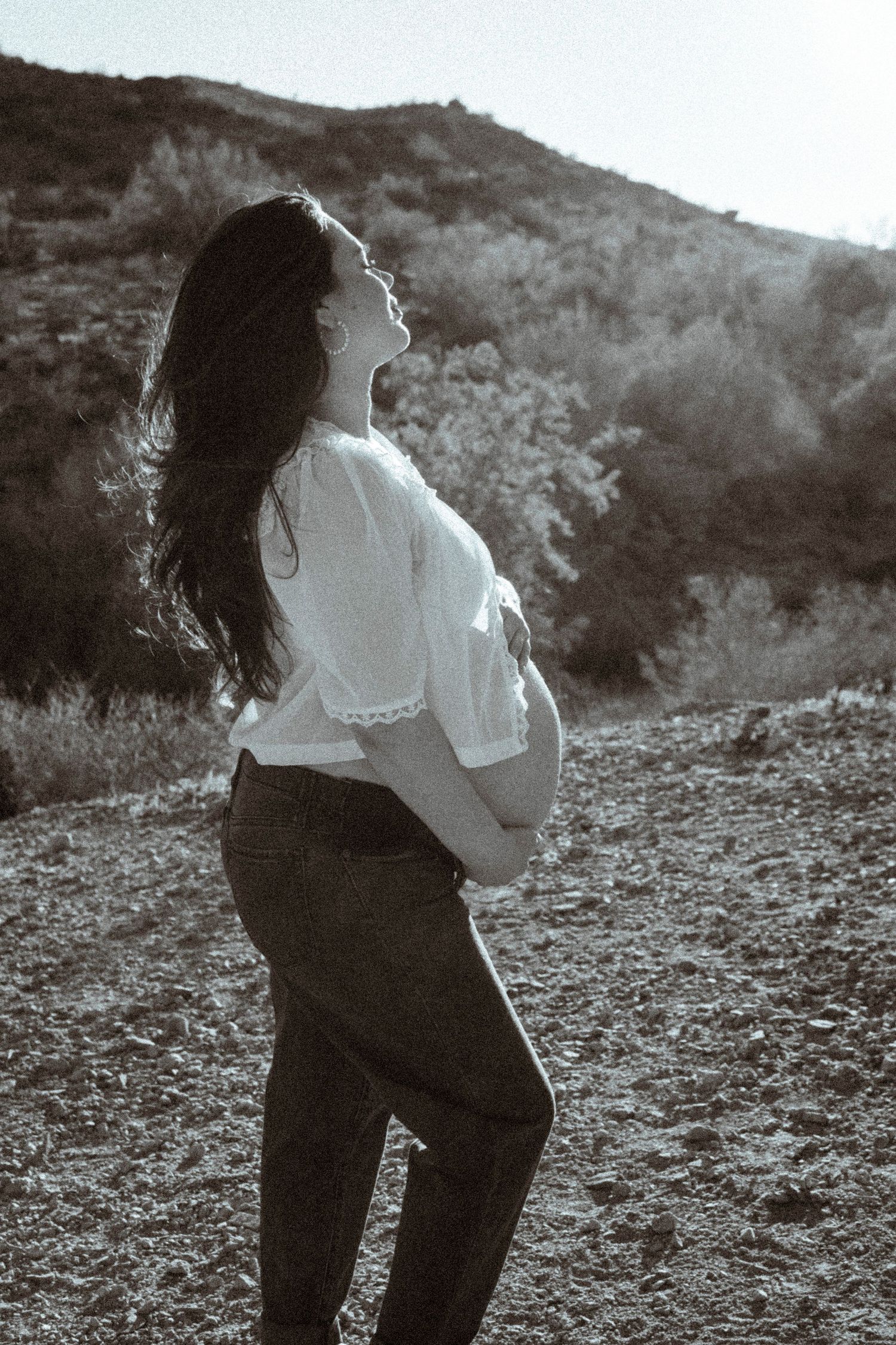 A silhouette of a pregnant woman standing against a mountain landscape in black and white.